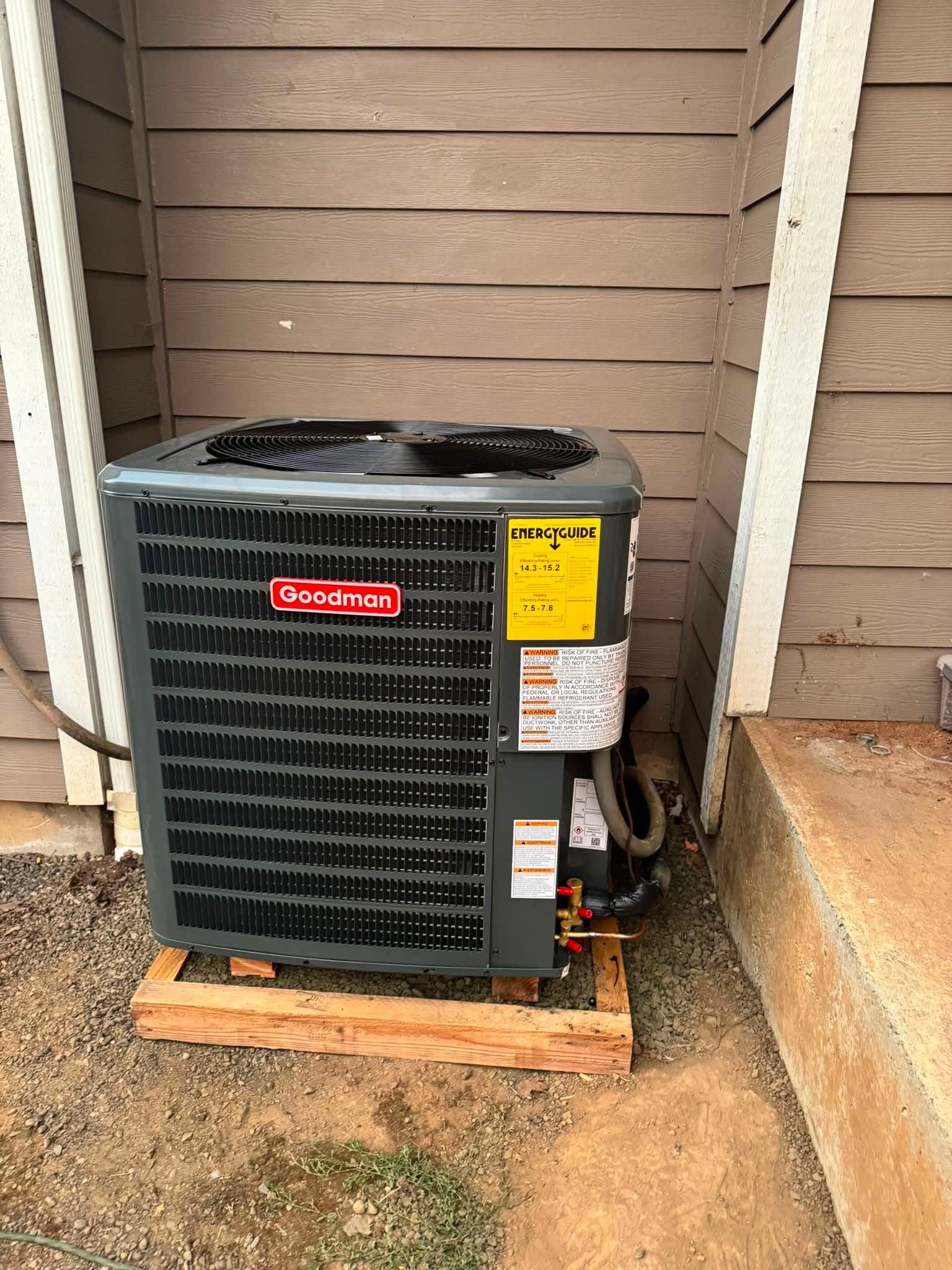 Outdoor air conditioner unit beside a house wall on a wooden pad
