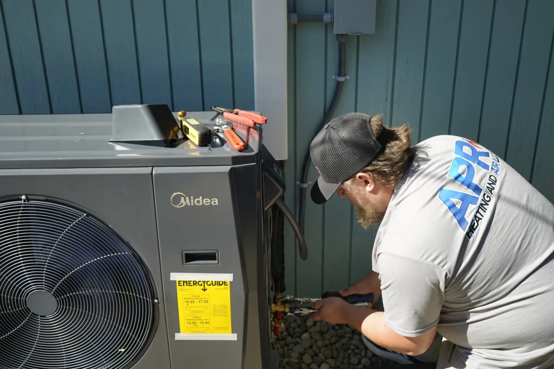 Technician inspecting an outdoor HVAC unit beside a house wall