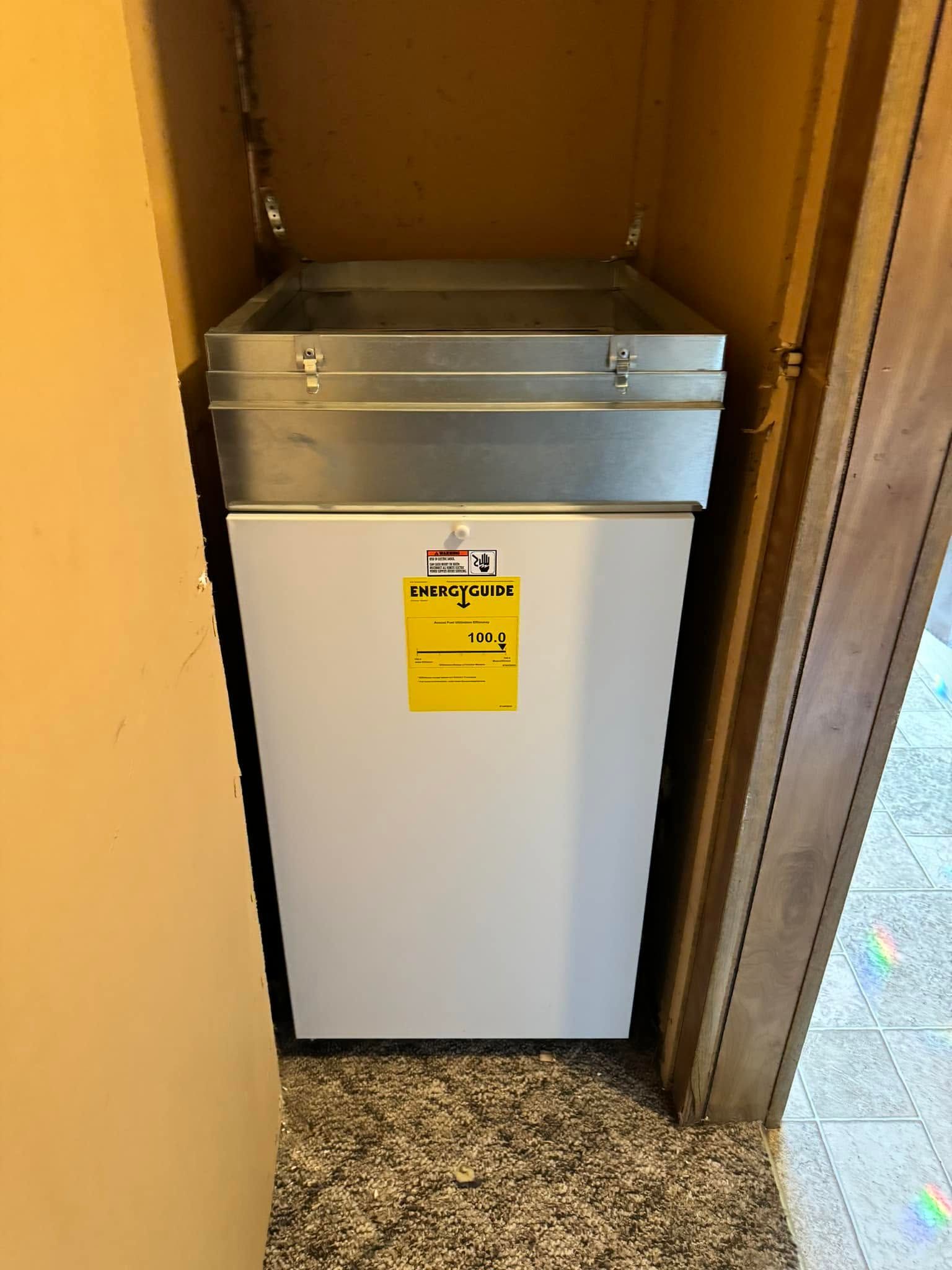 White refrigerator in a narrow hallway alcove with a yellow warning sign on the front.
