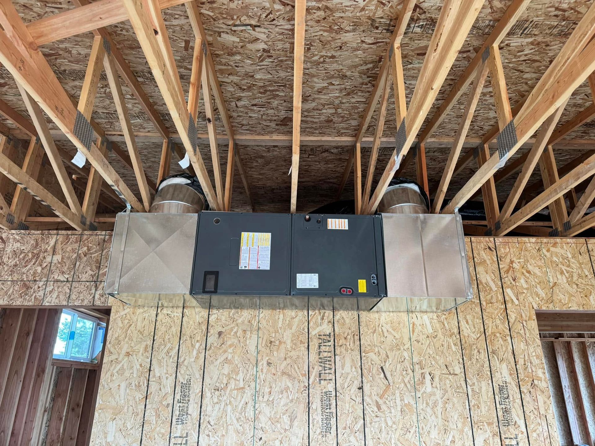 Ceiling-mounted HVAC unit in an unfinished room with exposed rafters and insulation