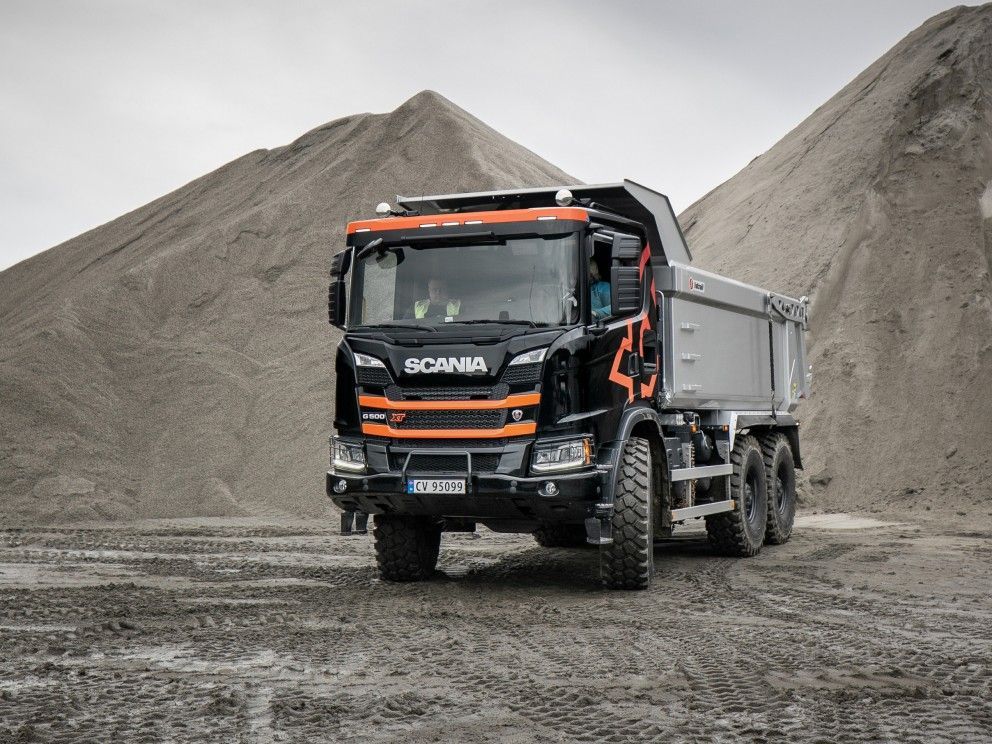 Un camion-benne noir et orange est garé devant un tas de terre.