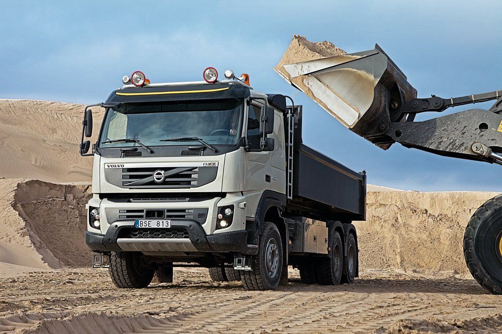 Un camion-benne est chargé de sable par un bulldozer.