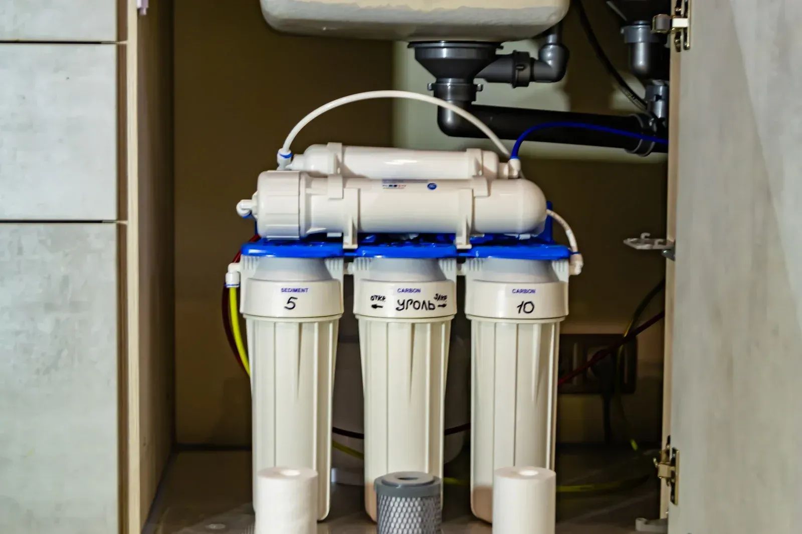 Under-sink water filter system with three white canisters and blue tubing in a cabinet