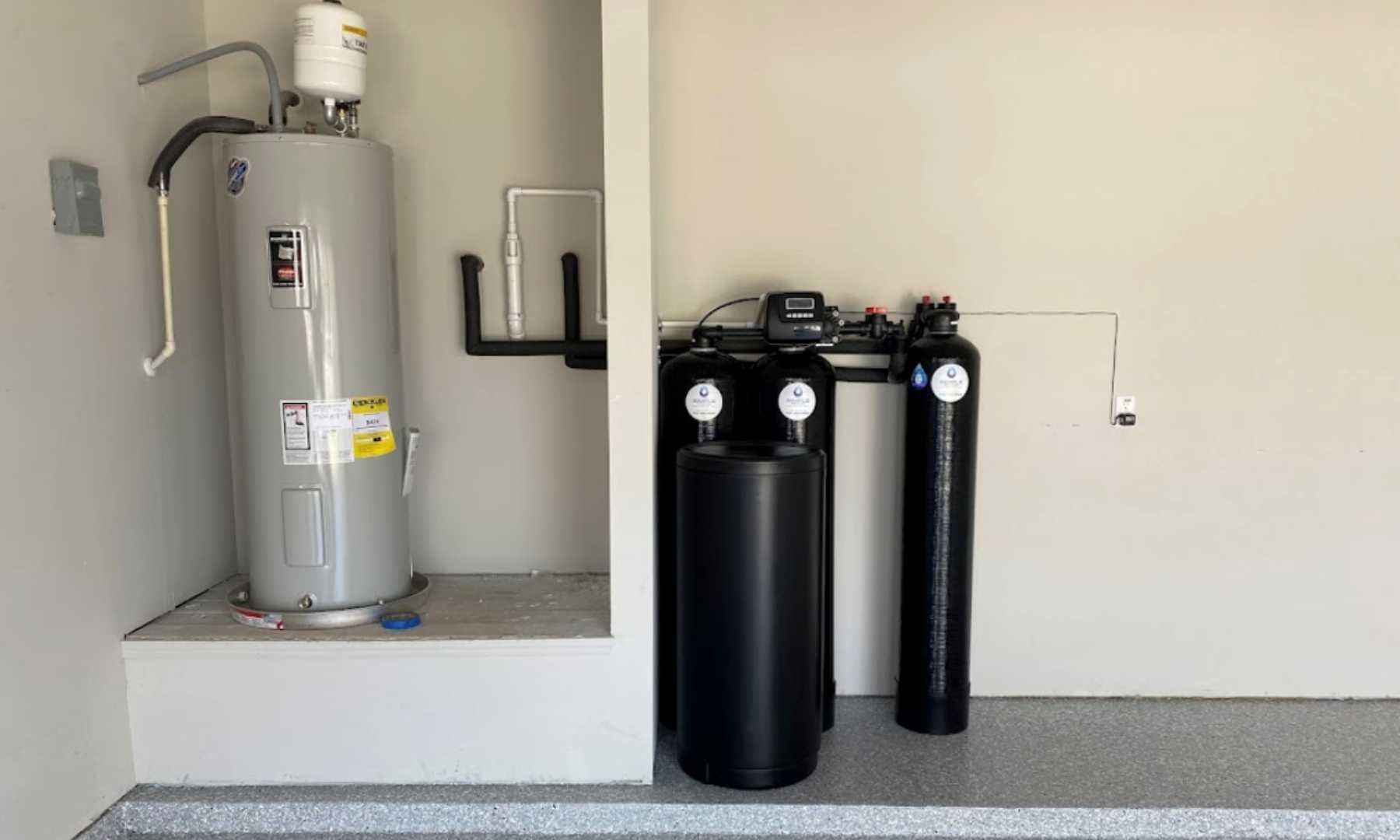A residential water heater and a black multi-stage water filtration system installed against a white wall in a garage.