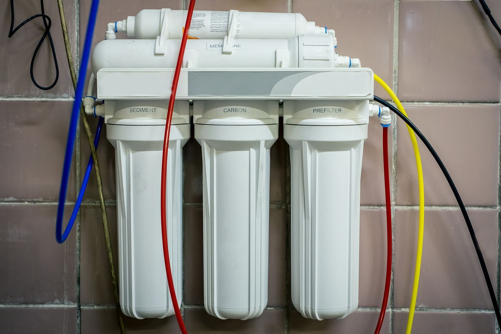 Water filtration system with four white canisters and colored hoses mounted against a tiled wall