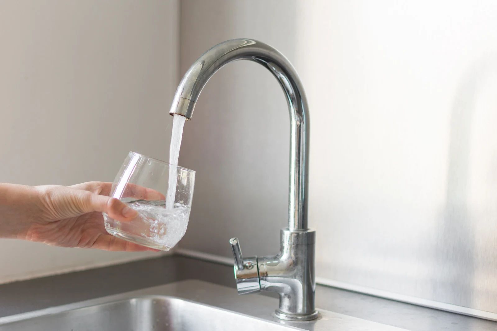 Hand filling a glass with water from a chrome kitchen faucet