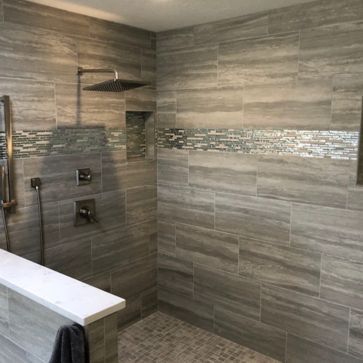 A bathroom with gray tiles and a shower head.
