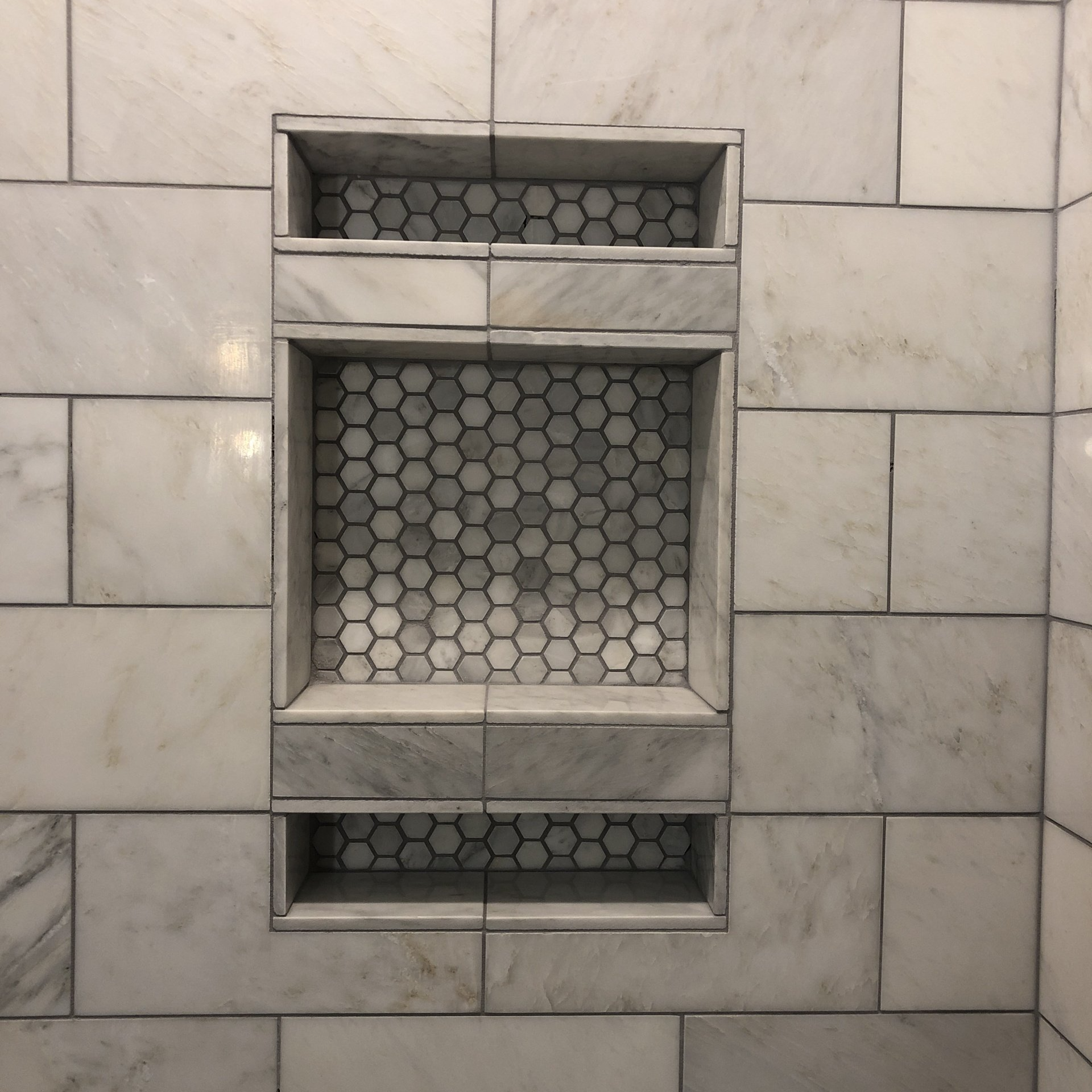 A shower niche in a bathroom with white tiles and honeycomb tiles.