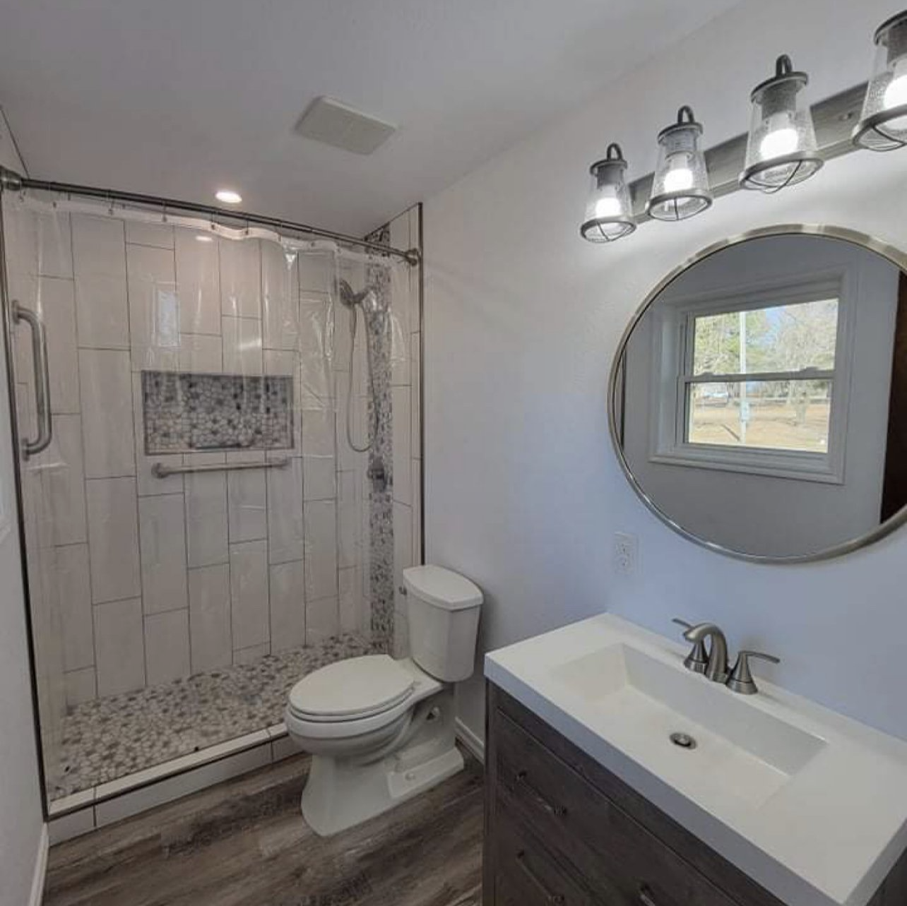 A bathroom with a toilet , sink , shower and mirror.