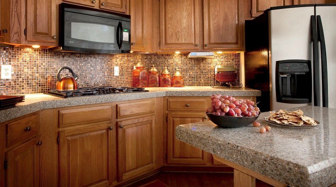 A kitchen with wooden cabinets , granite counter tops , a refrigerator , microwave , and stove.