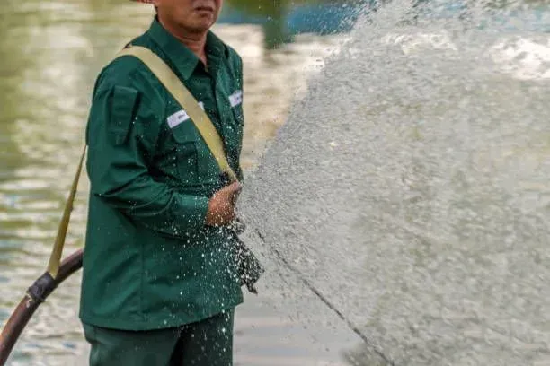 A person in a green uniform sprays a powerful stream of water from a hose.