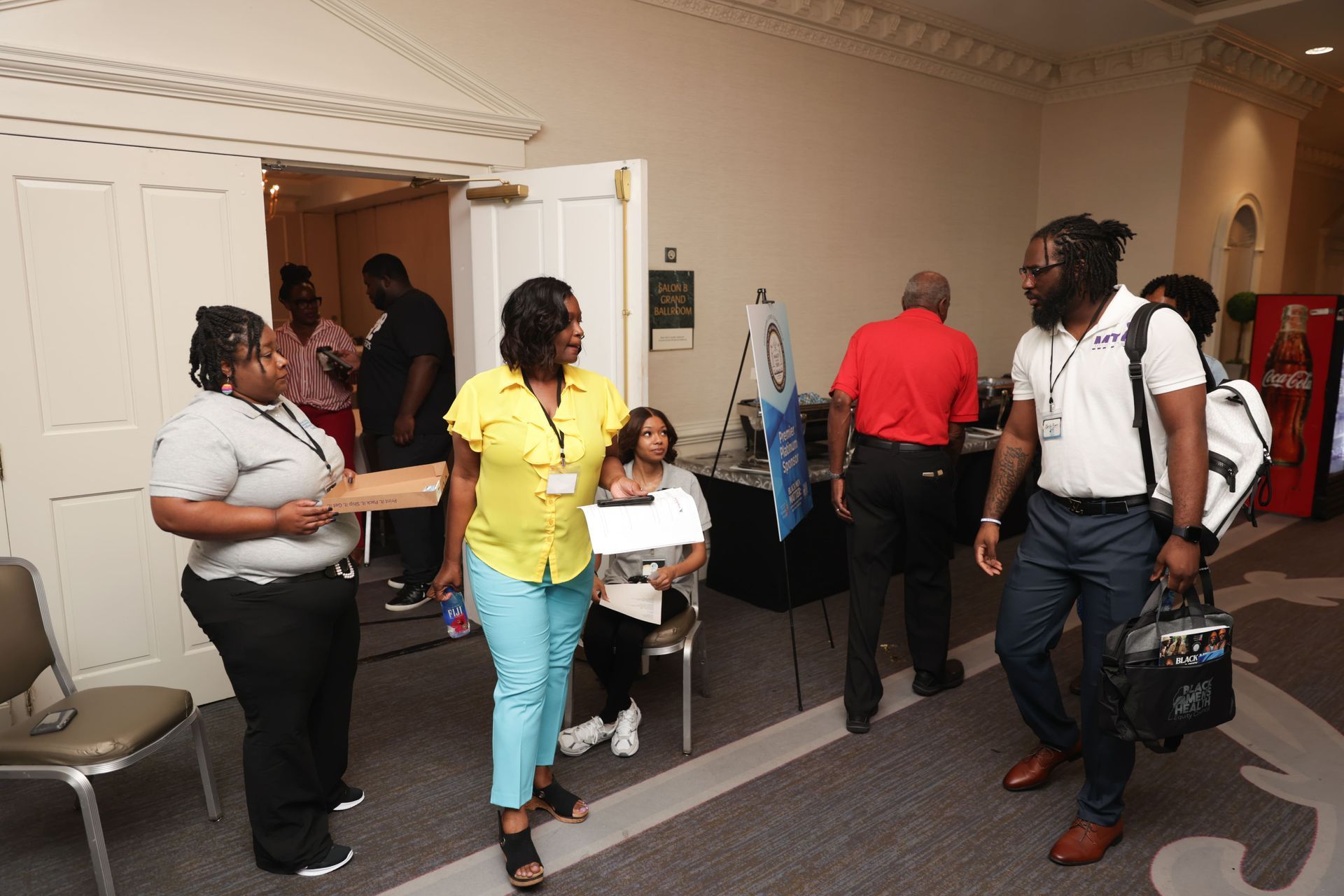 People at an event. Some are talking, others are walking. A table with brochures is set up.