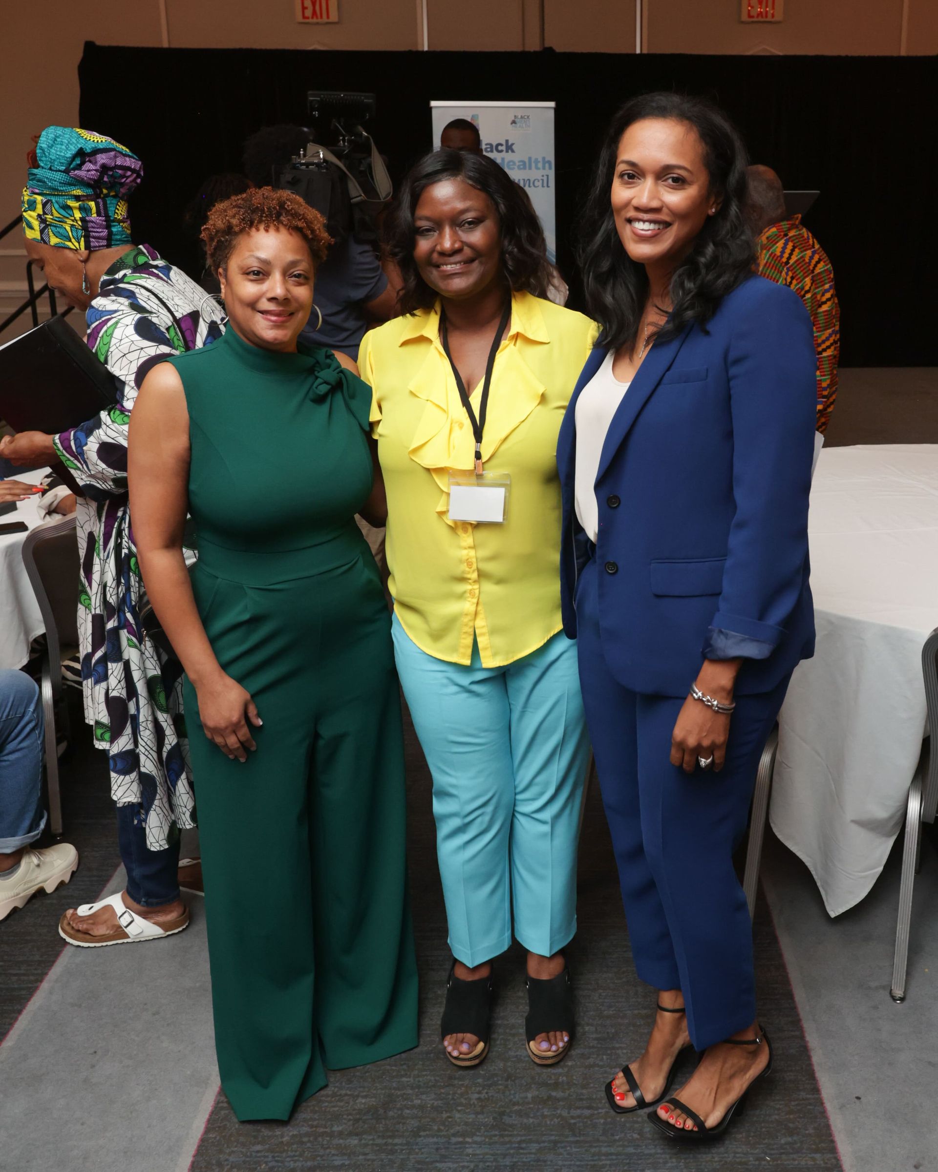 Dr. Melvin, Marilyn Reed | Three women smiling at a conference. The woman on the left in green, center in yellow, right in blue suit.