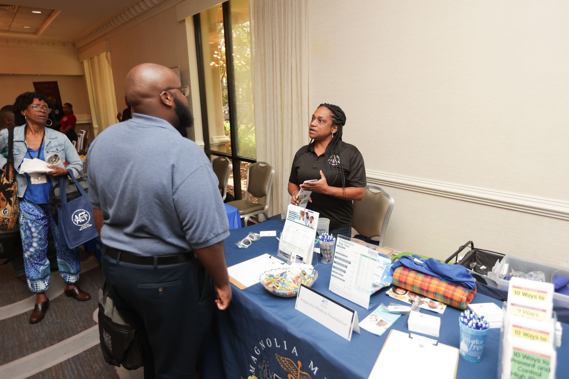 Person speaking at a booth at an event with brochures and a table cloth.