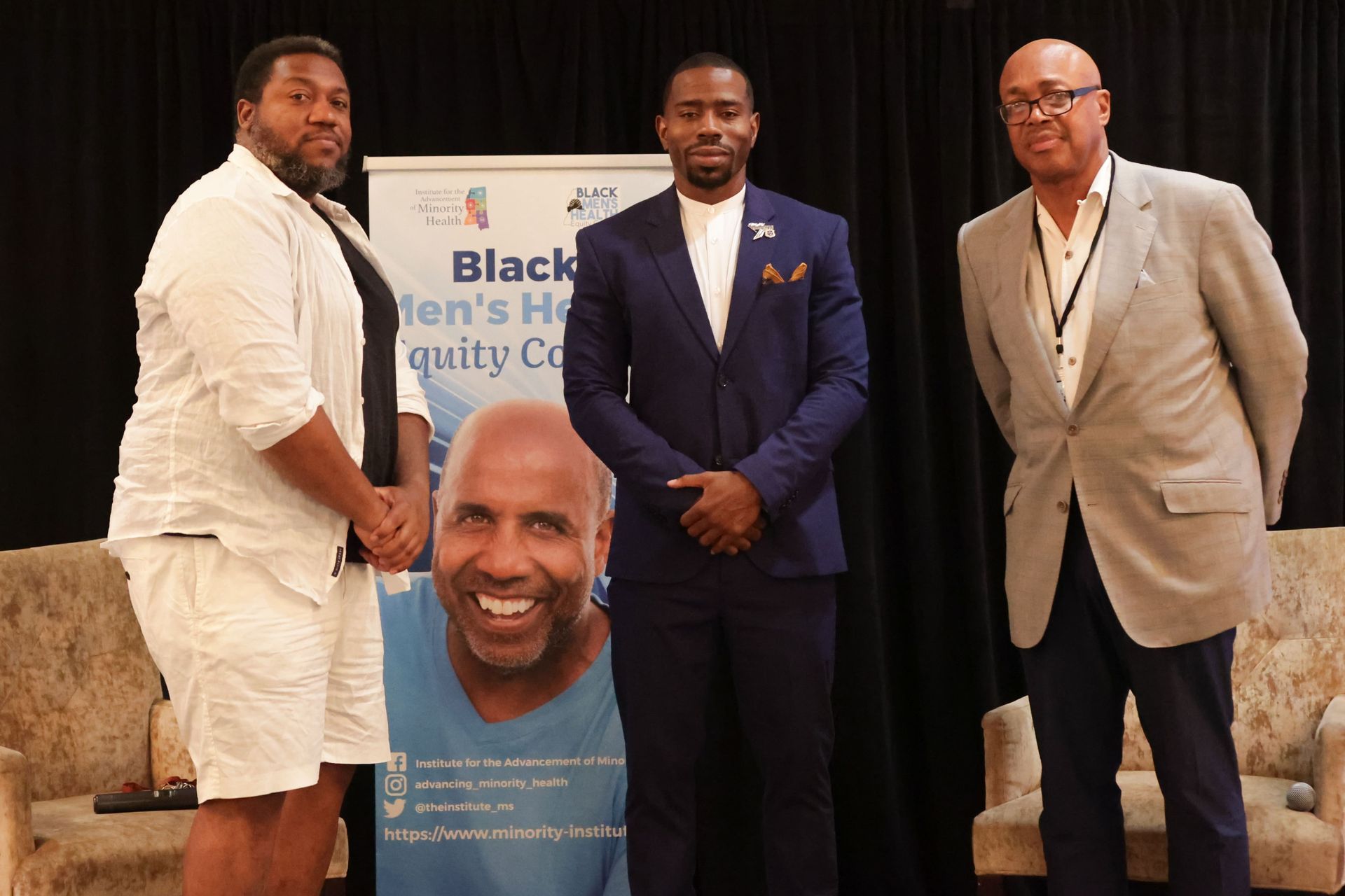 Three men stand in front of a banner promoting Black Men's Health.