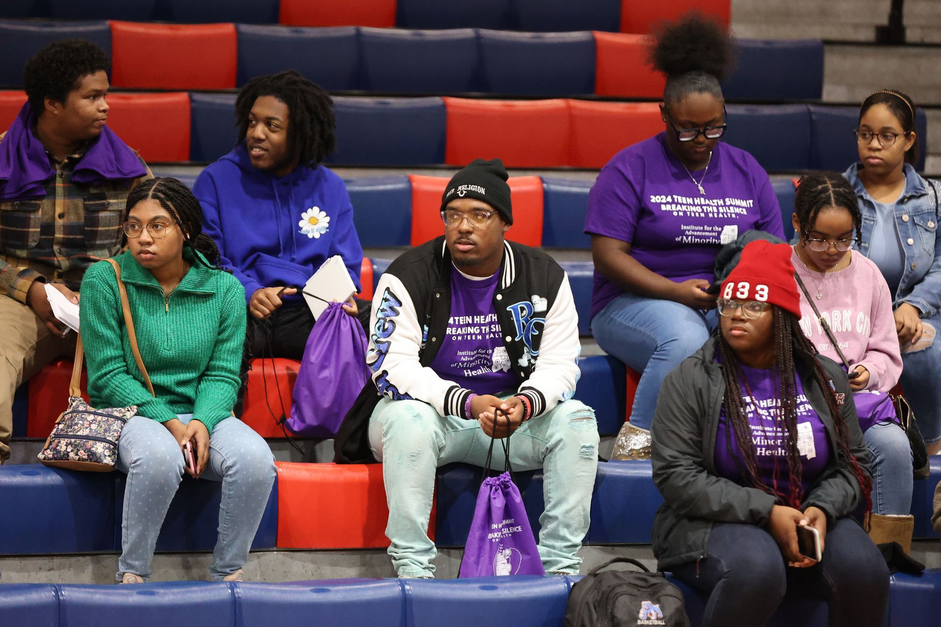 People seated in bleachers, some wearing purple shirts and hats, watching an event.