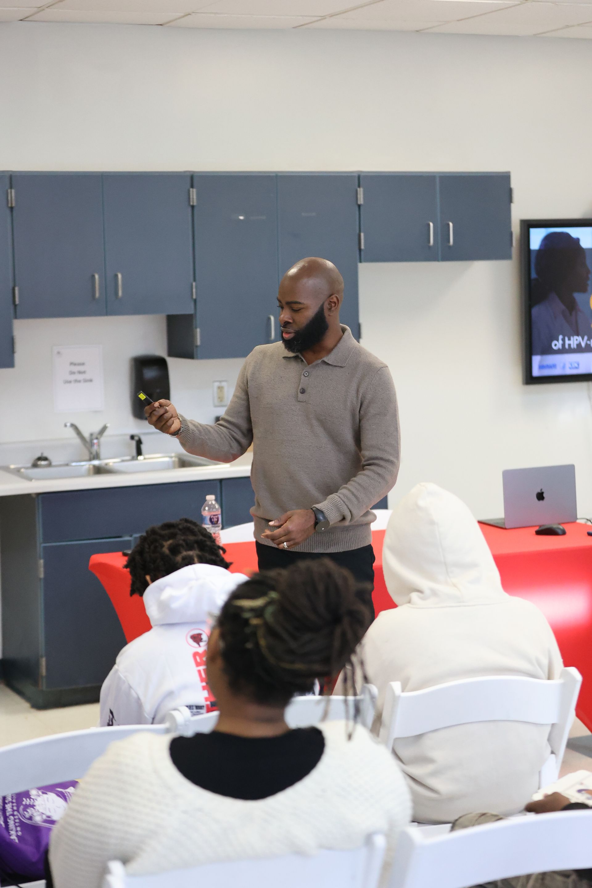 A man gestures during a presentation to a small audience in a room.