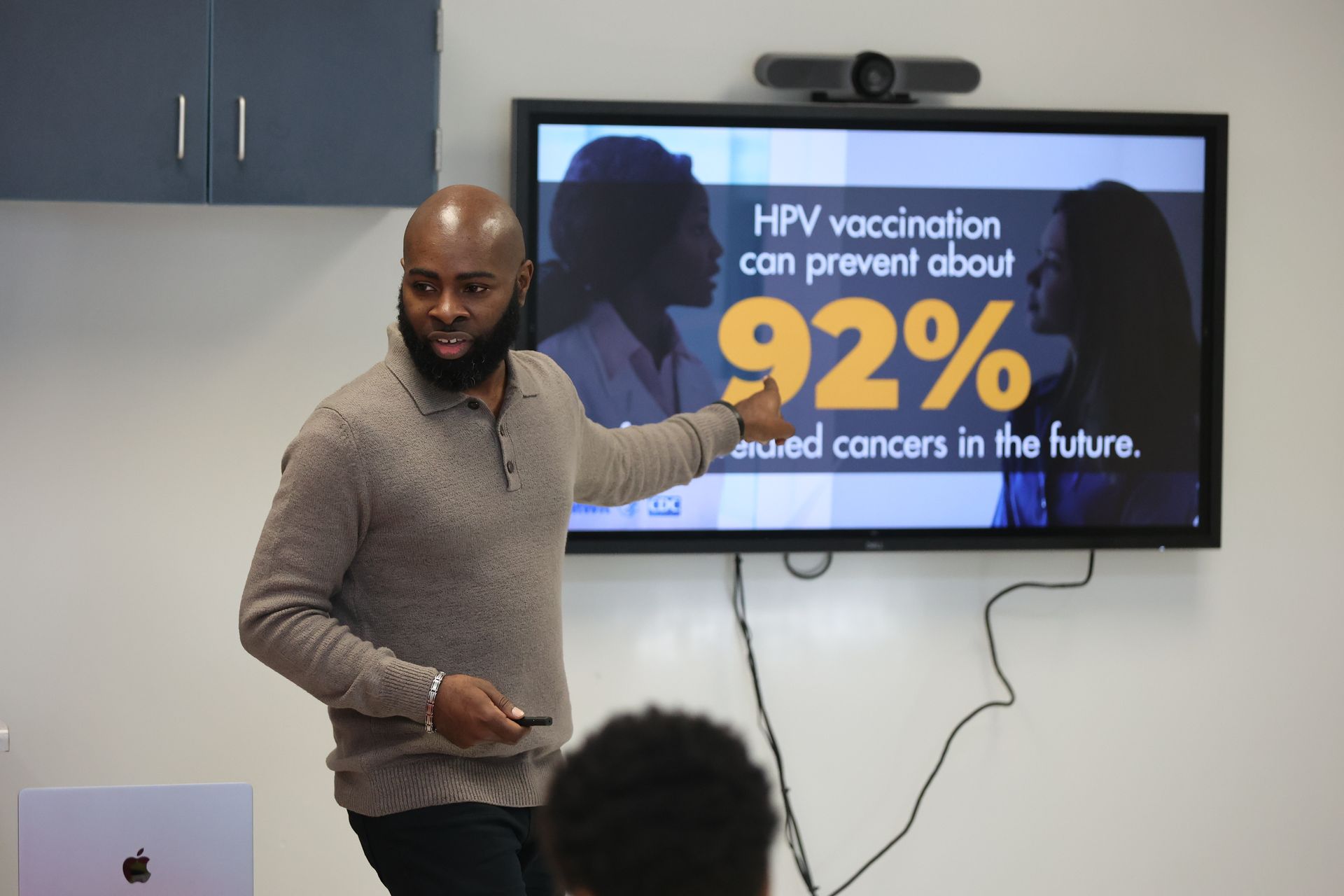 Man points to a screen with HPV vaccine statistics. Screen shows image and text: