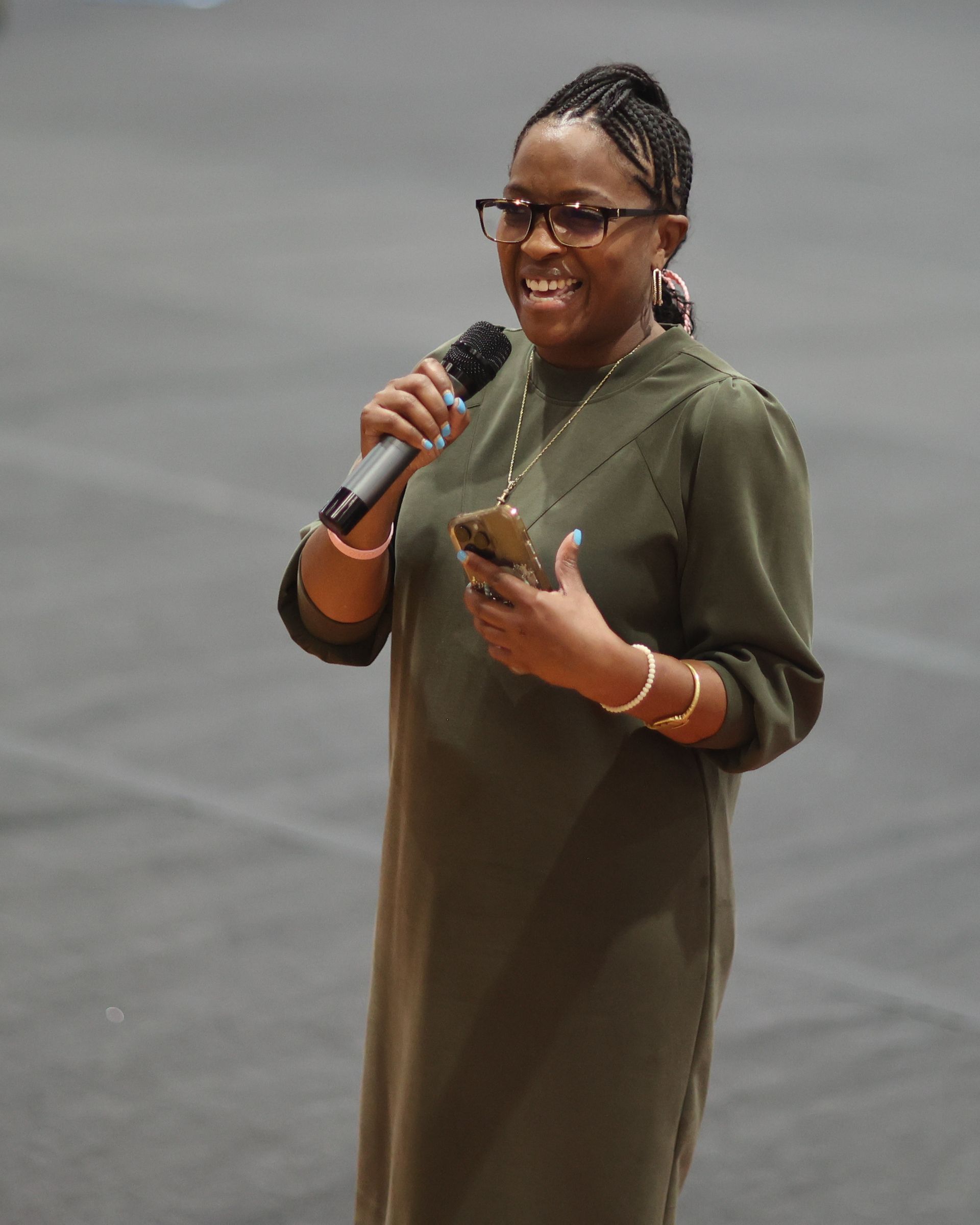 Woman in a green dress speaks into a microphone, smiling, holding a phone.