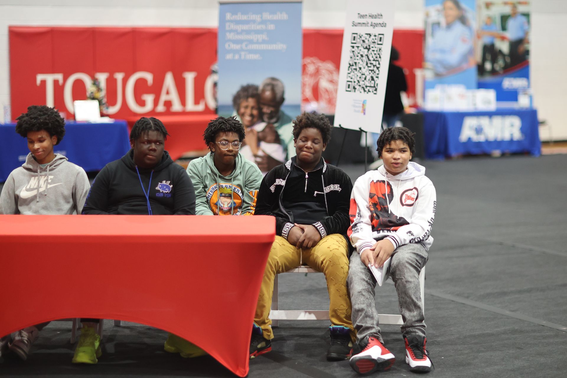 Five people sitting at a red table at a fair, Tougaloo banner in the background.