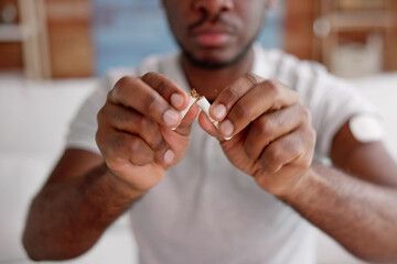 Man breaking a cigarette in half, signifying quitting smoking. White shirt, close-up.