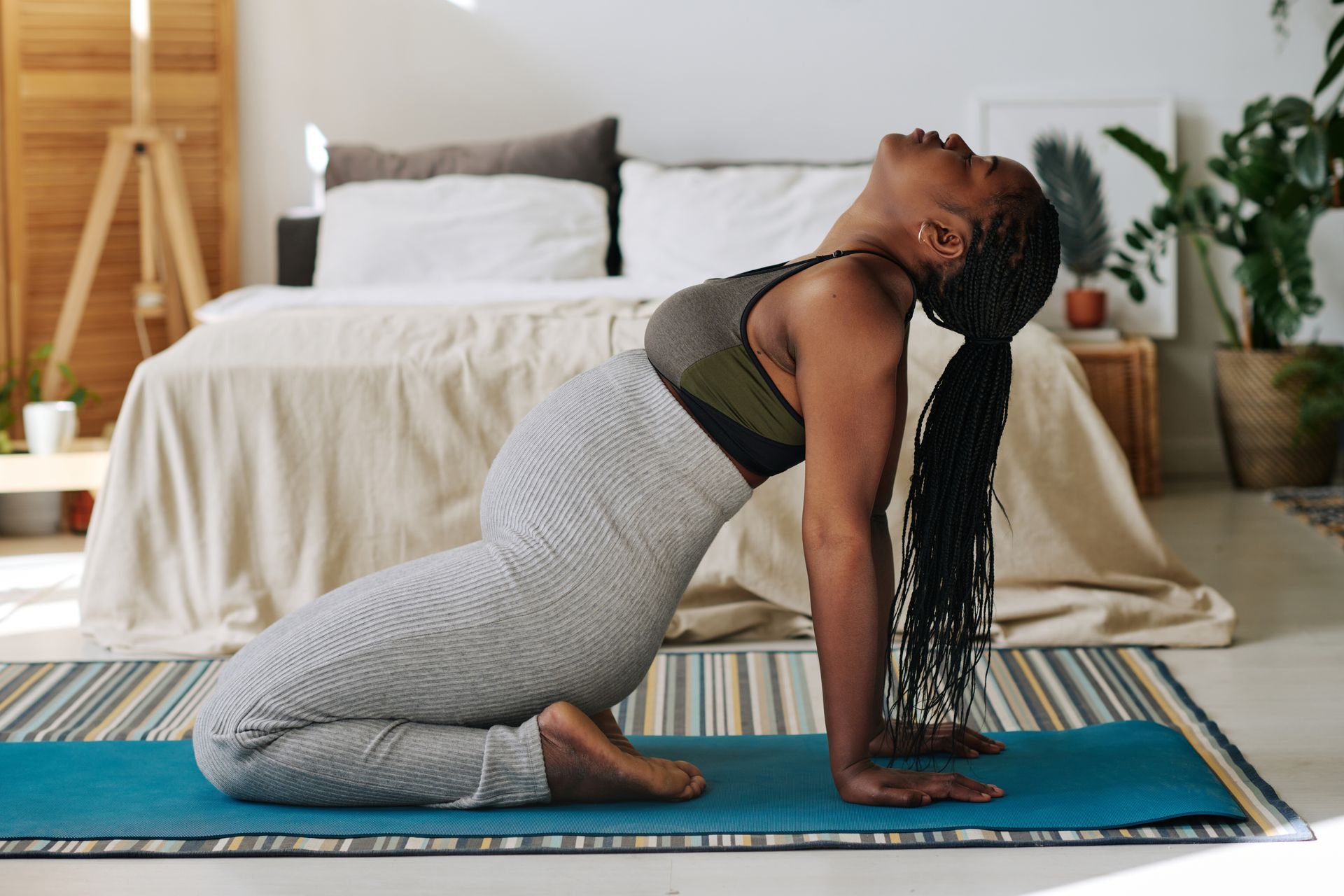 Woman in yoga pose on a blue mat, arched back, eyes closed, in a bedroom.