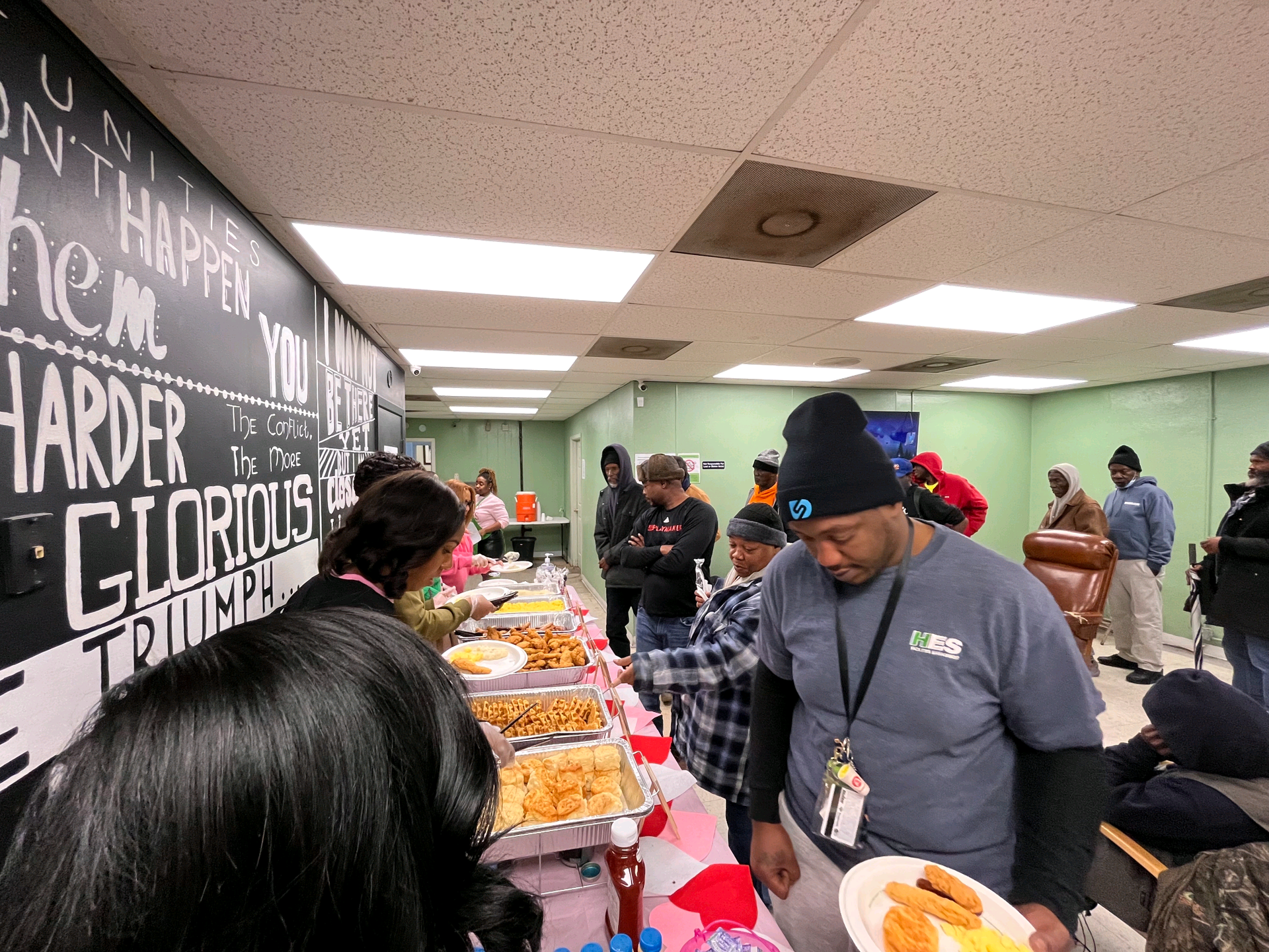 People serving themselves from a buffet in a brightly lit room. A sign reads, 