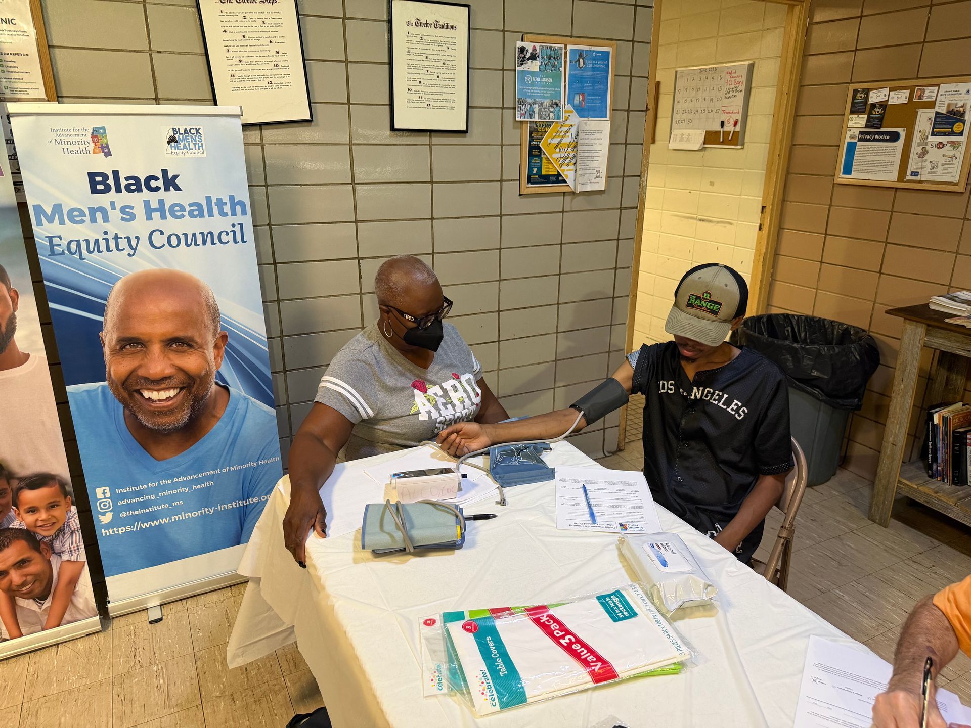 Two people sit at a table in a hallway booth for Black Men’s Health Equity, with flyers and pamphlets displayed.