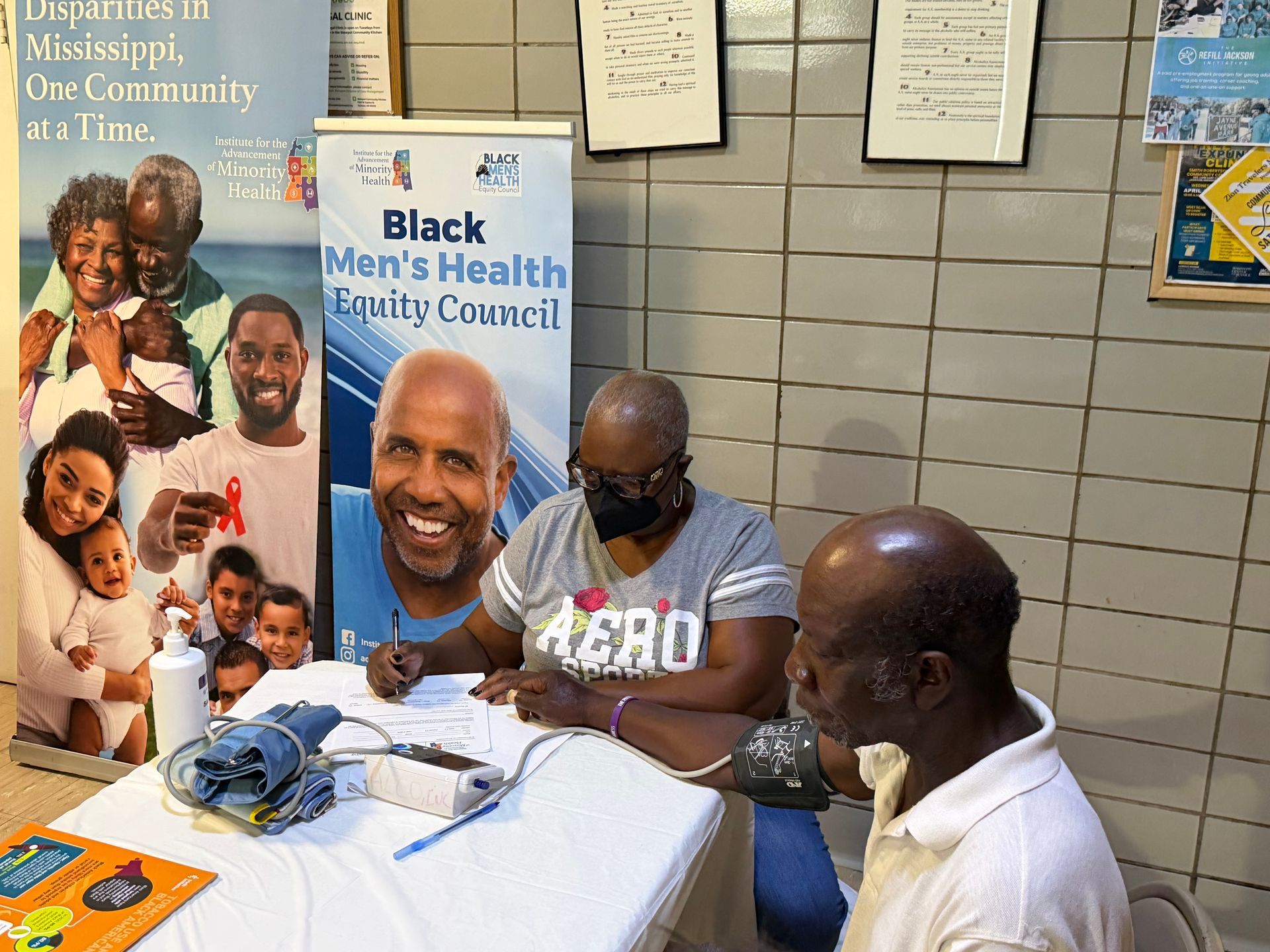 Men seated at a table with Black Men's Health Council banner and informational materials at community event