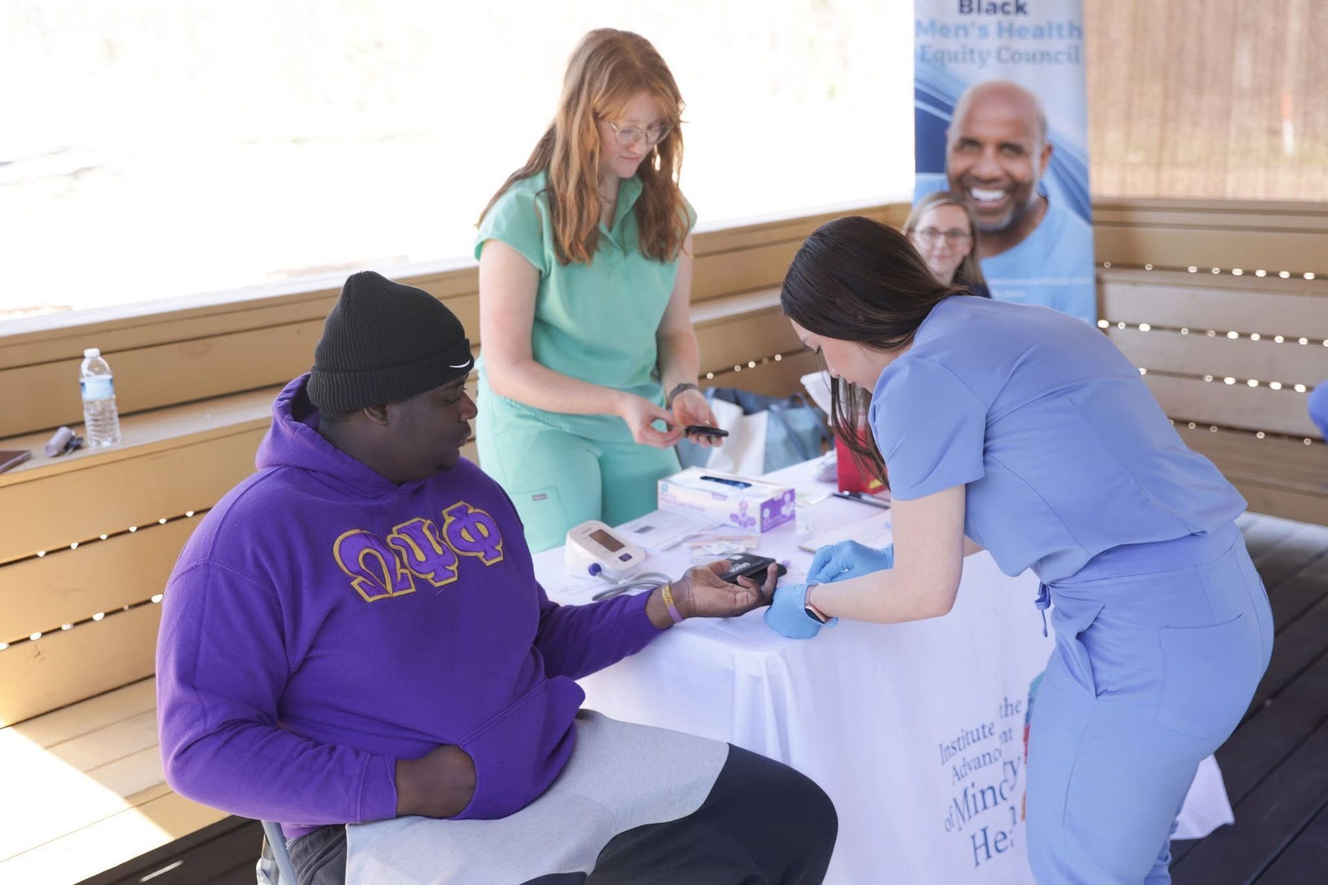A man in purple hoodie has his blood pressure checked by a healthcare worker at an outdoor health clinic.