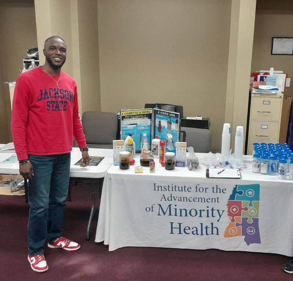 Man in red shirt stands behind a table with health products.