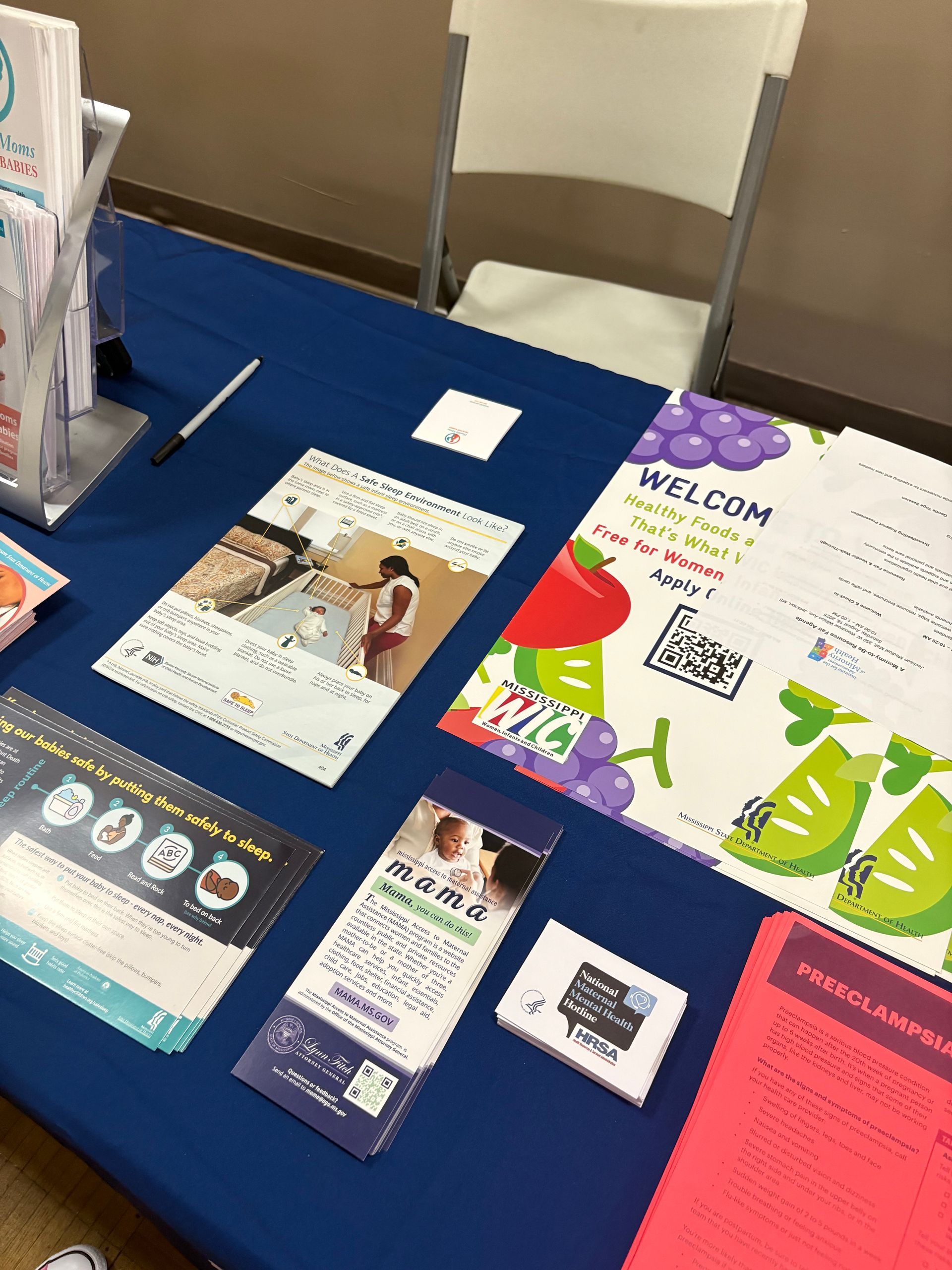 Table with brochures and promotional materials at an event, with a chair in the background.