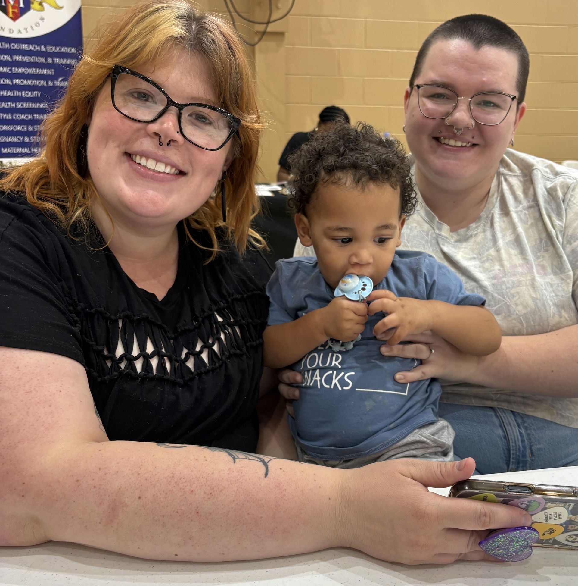 Ways You & Your Group Can Help Three people smiling at a table, with a child holding a snack in the center.