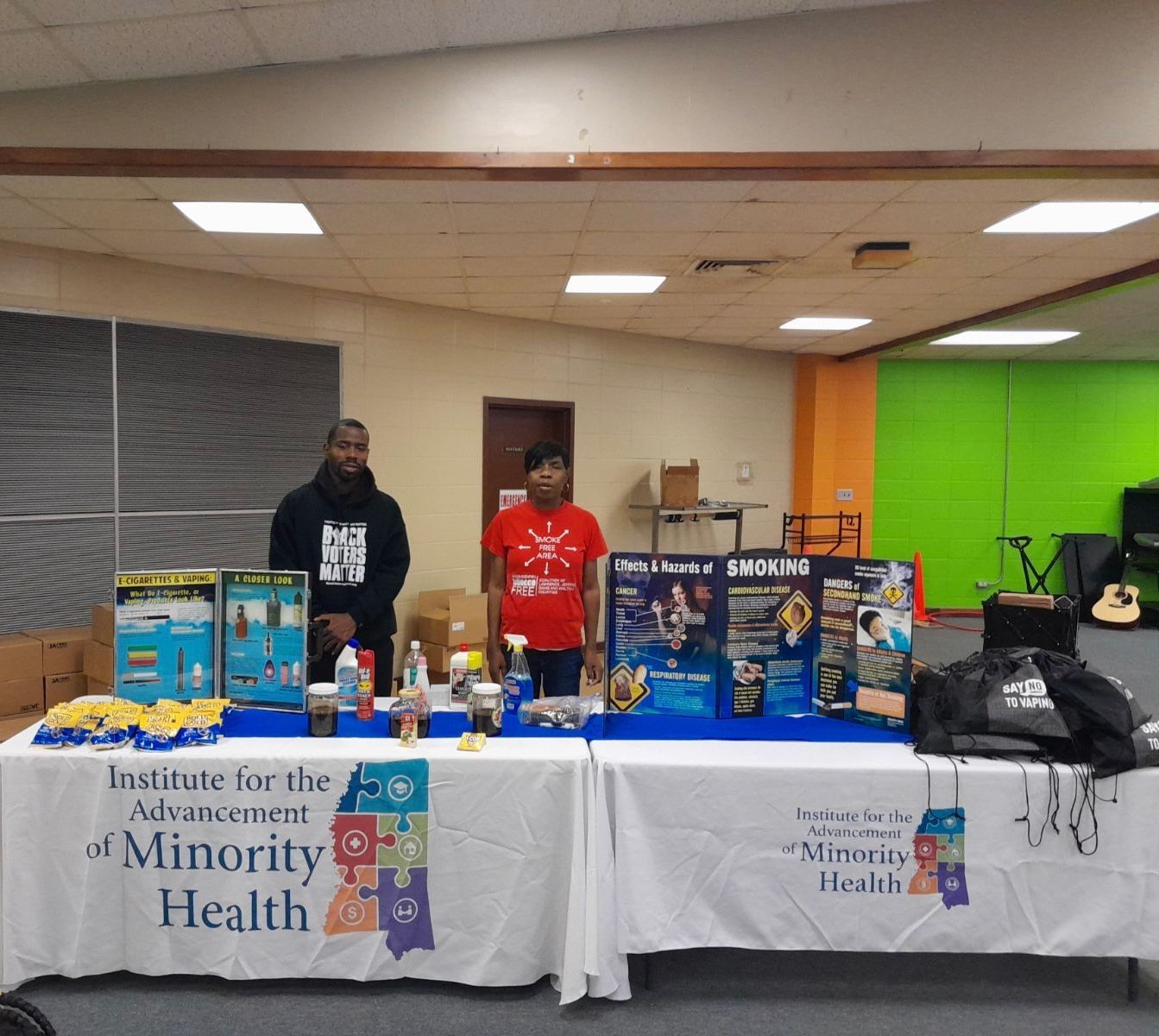 Two people stand behind a table displaying Institute for the Advancement of Minority Health products.