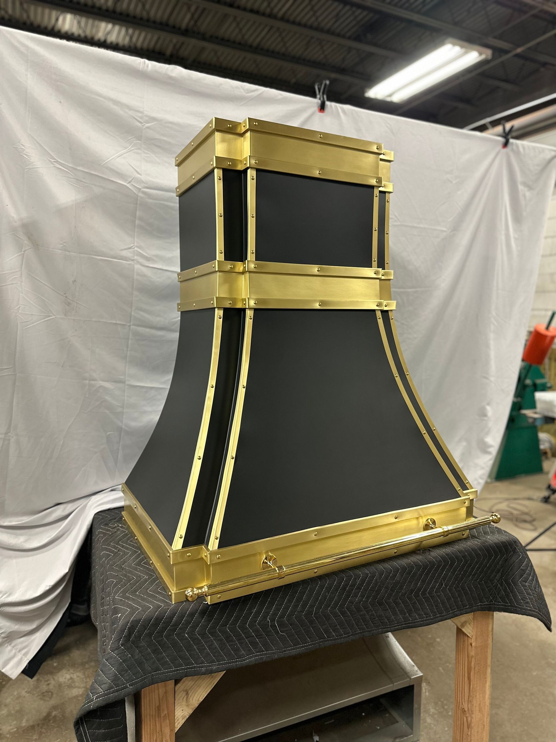 Black-and-gold decorative column or pedestal on a worktable in a workshop, with white draped backdrop