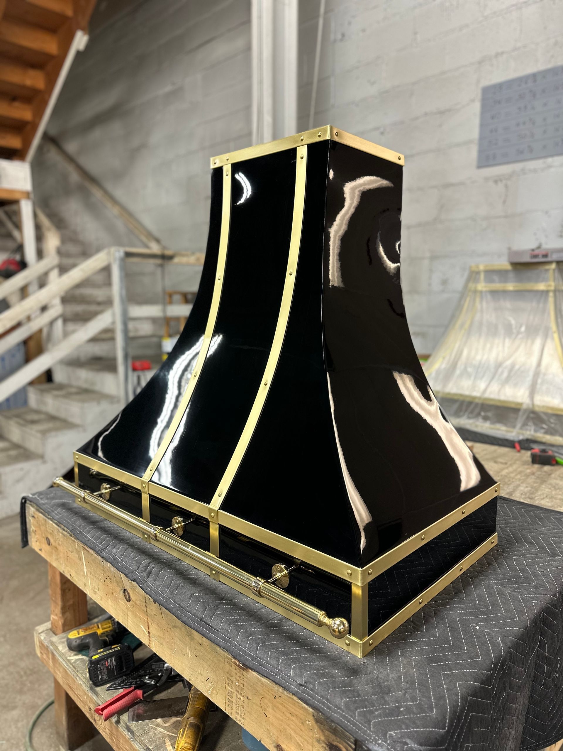 Black glossy sculptural object with gold trim on a workbench in a workshop