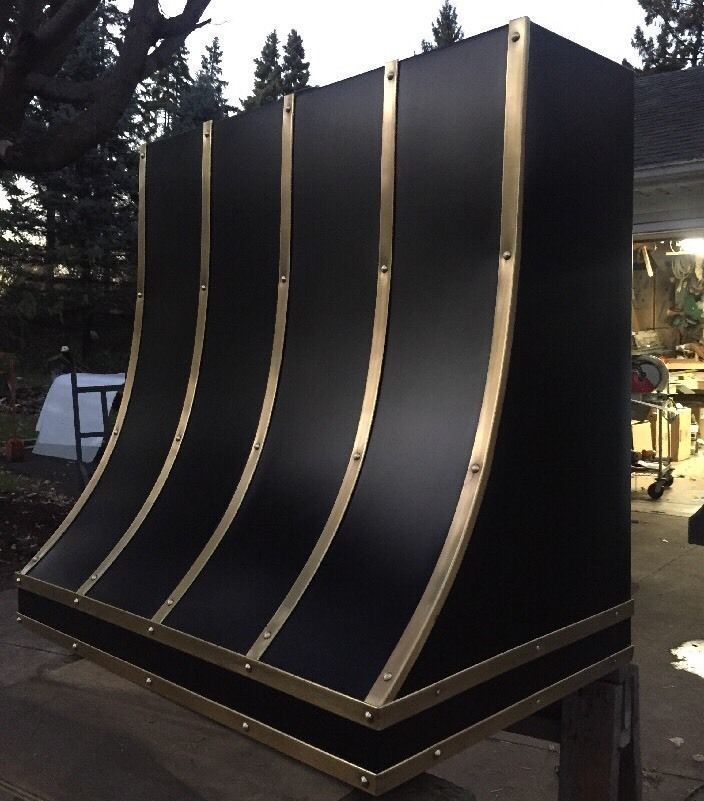 Large black curved metal structure with rivets, viewed outdoors at dusk.