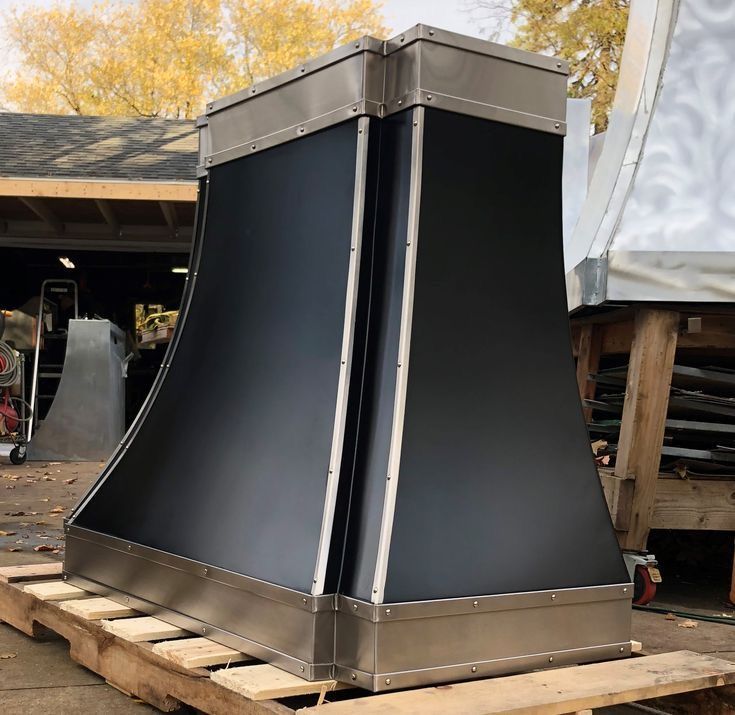 Large black metal industrial hood or enclosure with silver trim on a pallet outdoors