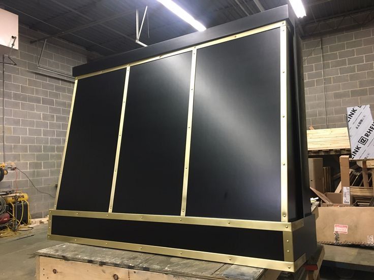 Large black industrial cabinet or enclosure with gold trim in a warehouse workshop