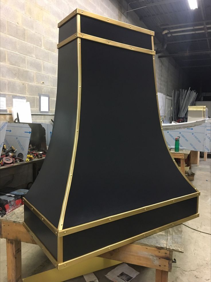 Black tapered chimney hood with gold trim in a workshop