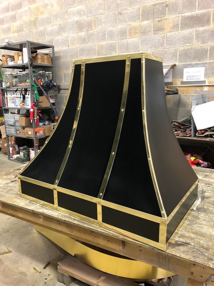 Black, gold-trimmed tapered hood or cabinet on a workbench in a workshop
