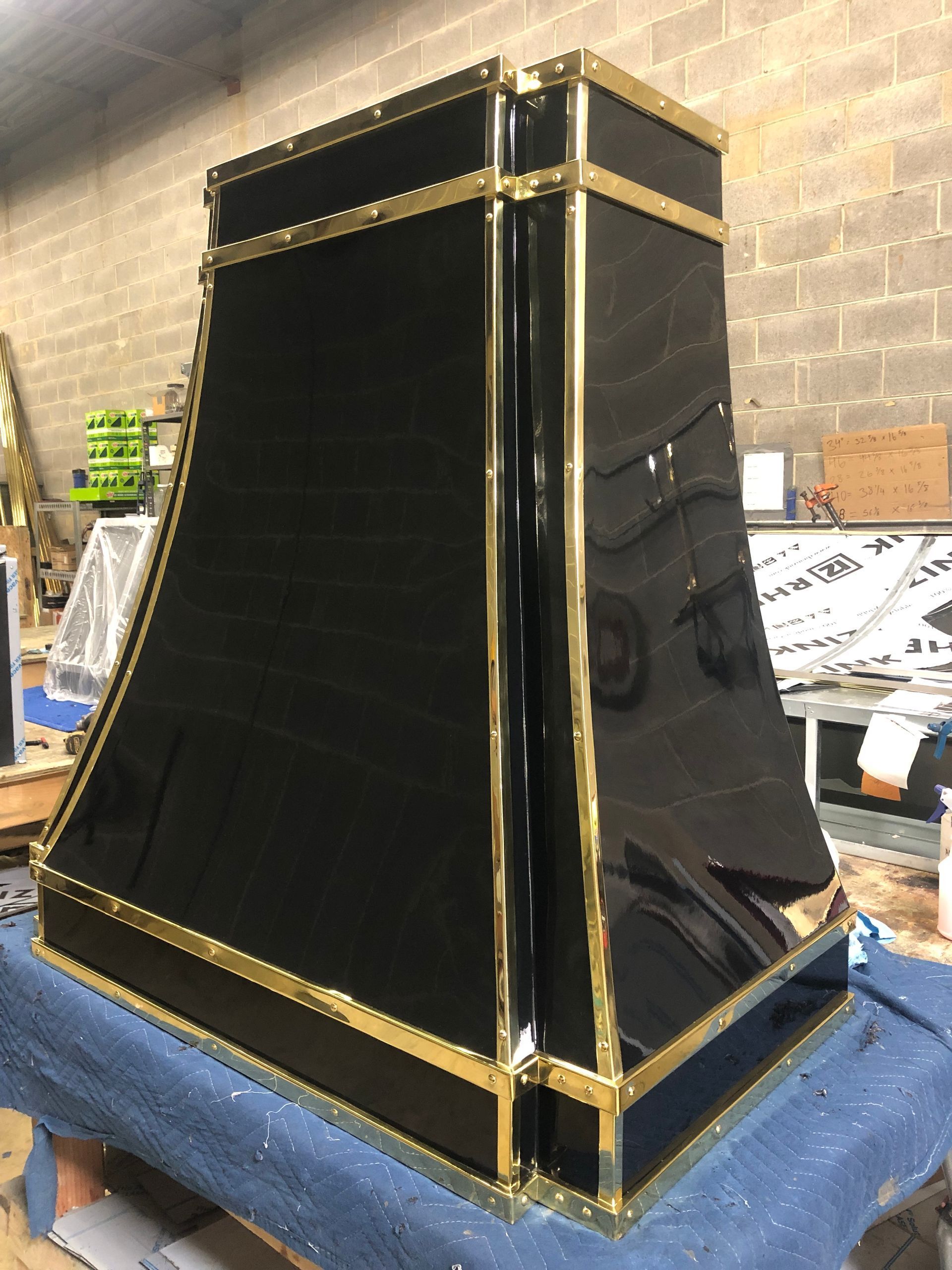 Black glossy pyramid-shaped object with gold trim on a blue tarp in a workshop.