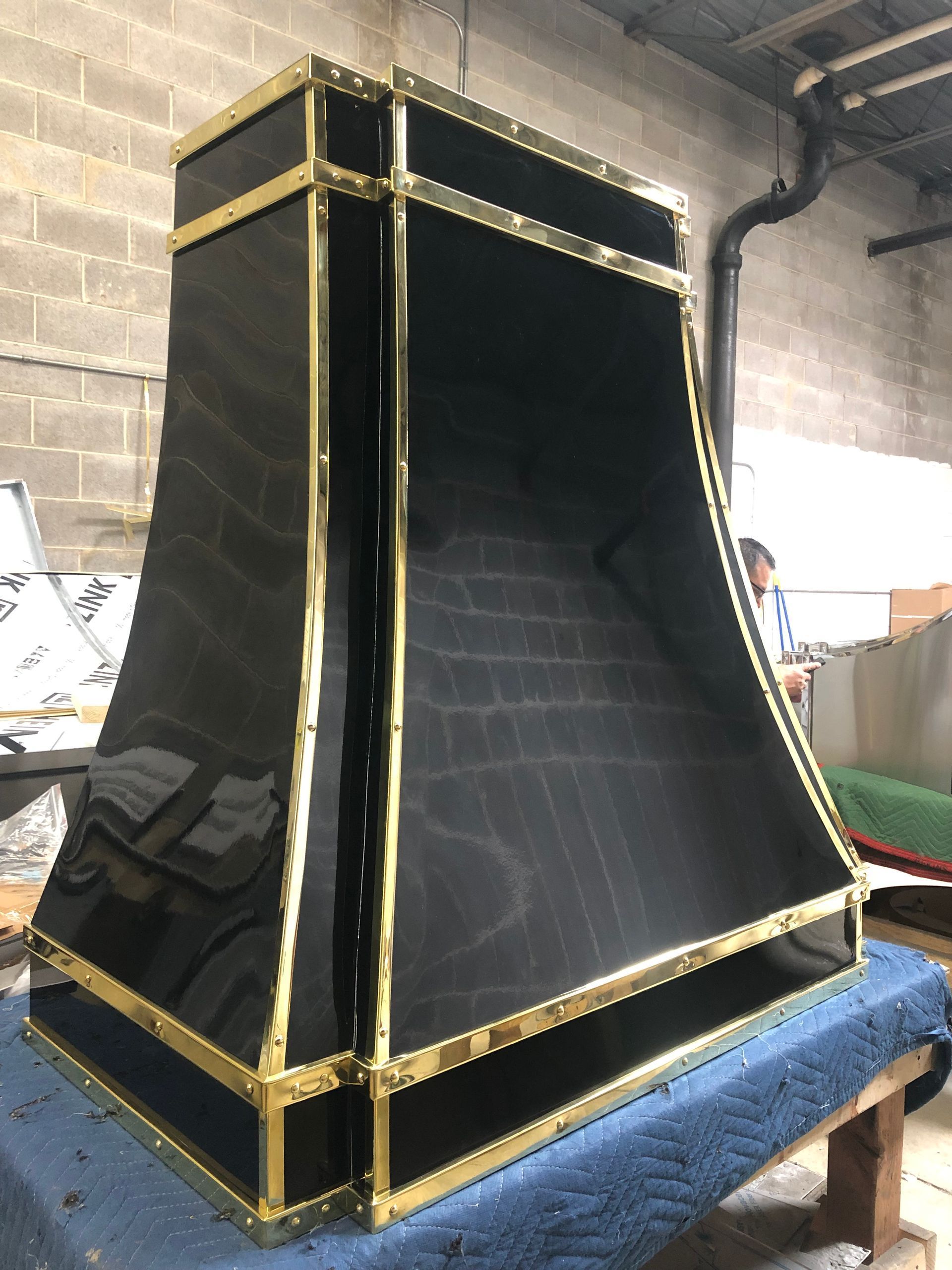 Large black-and-gold speaker enclosure in a workshop, sitting on a blue padded table.