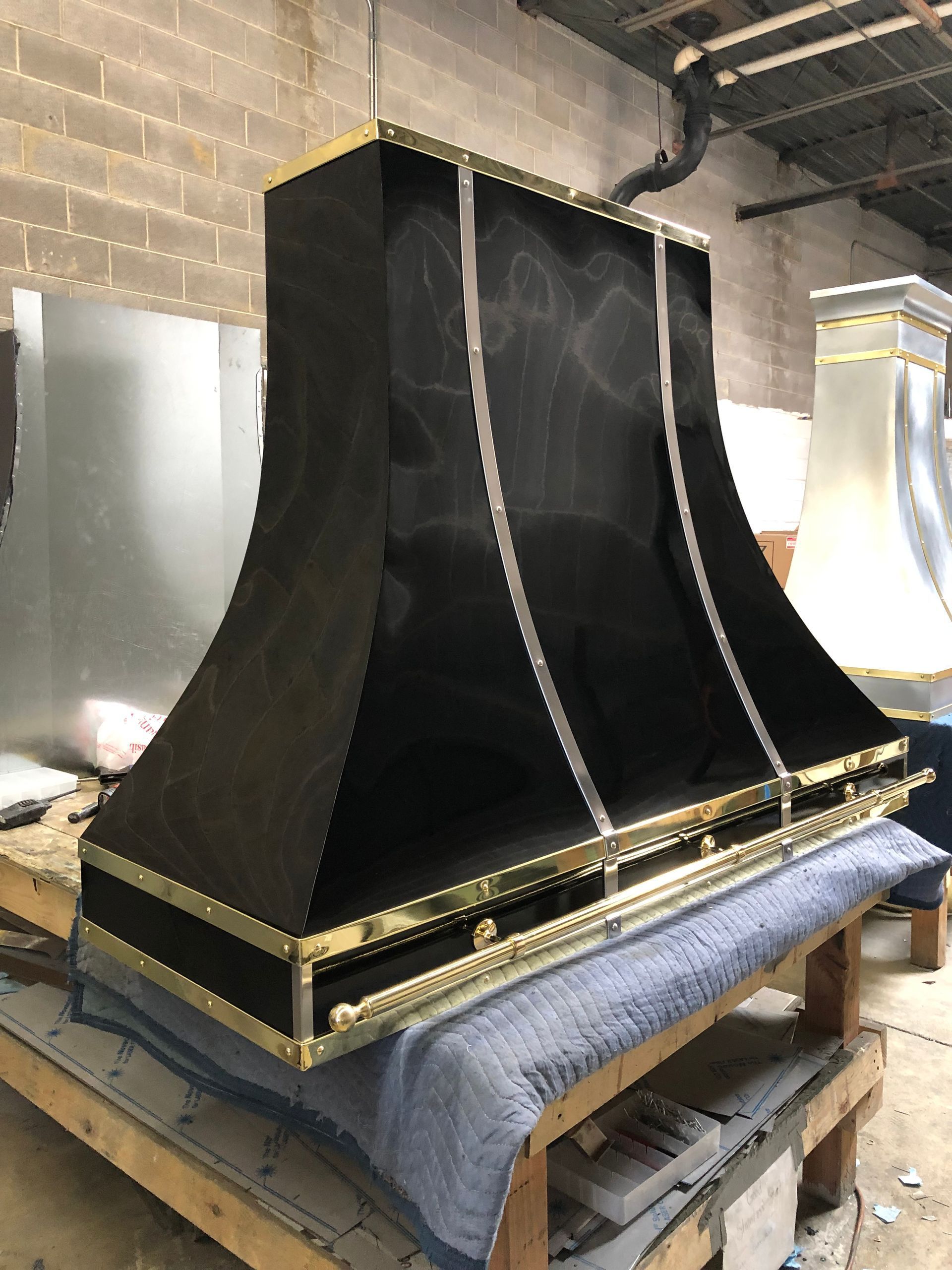 Large black vent hood or fireplace surround in a workshop, trimmed with gold accents, on a covered workbench
