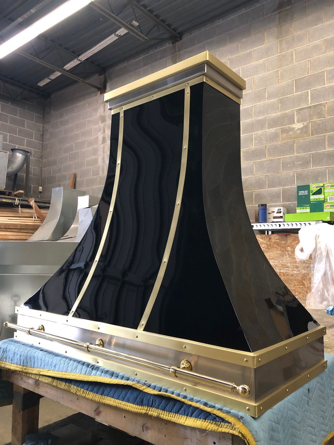 Large black carved architectural pedestal with gold trim in a workshop, resting on a workbench.