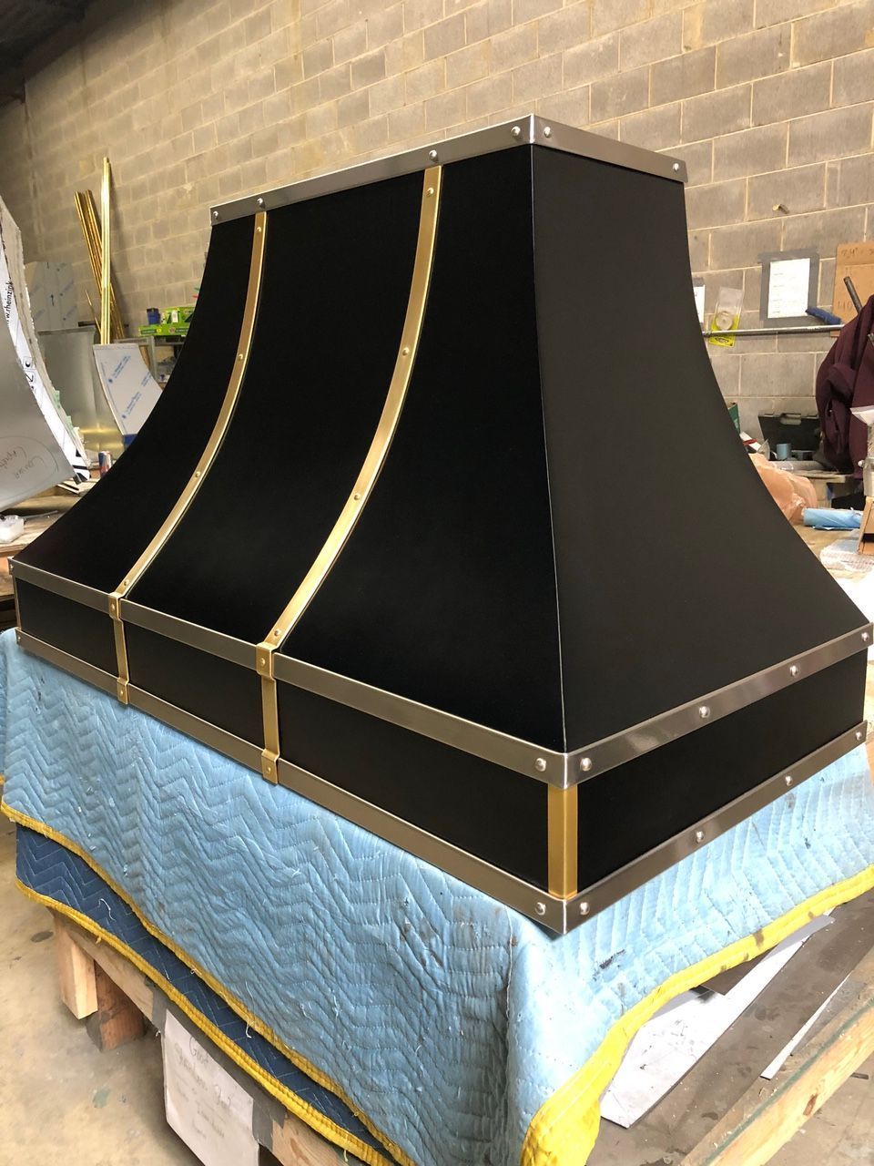 Black angular furniture piece on a workbench, with gold trim and a blue cover in a workshop