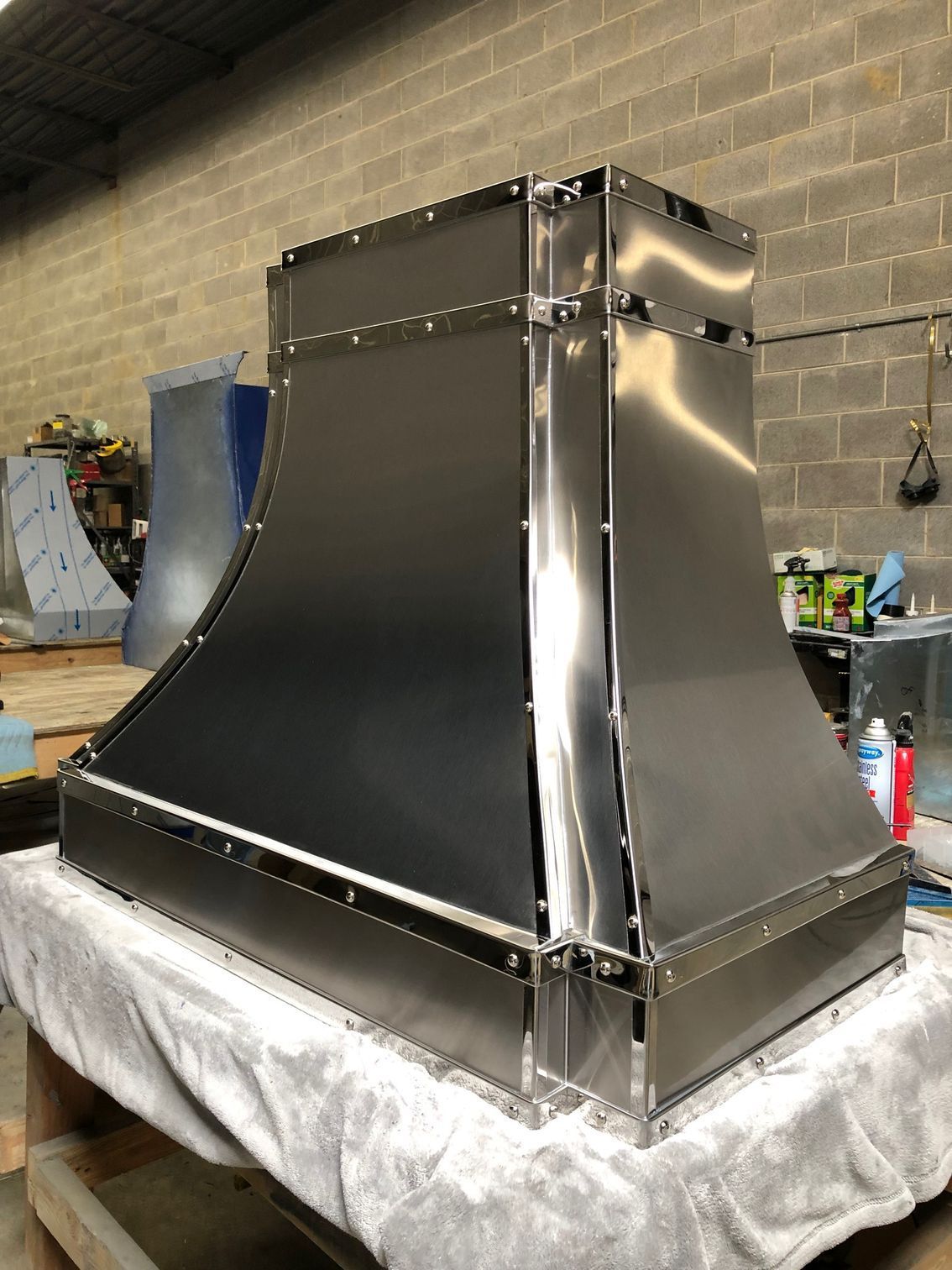 Black metal hood or enclosure on a workbench in a garage, with shiny chrome trim and brick wall behind.