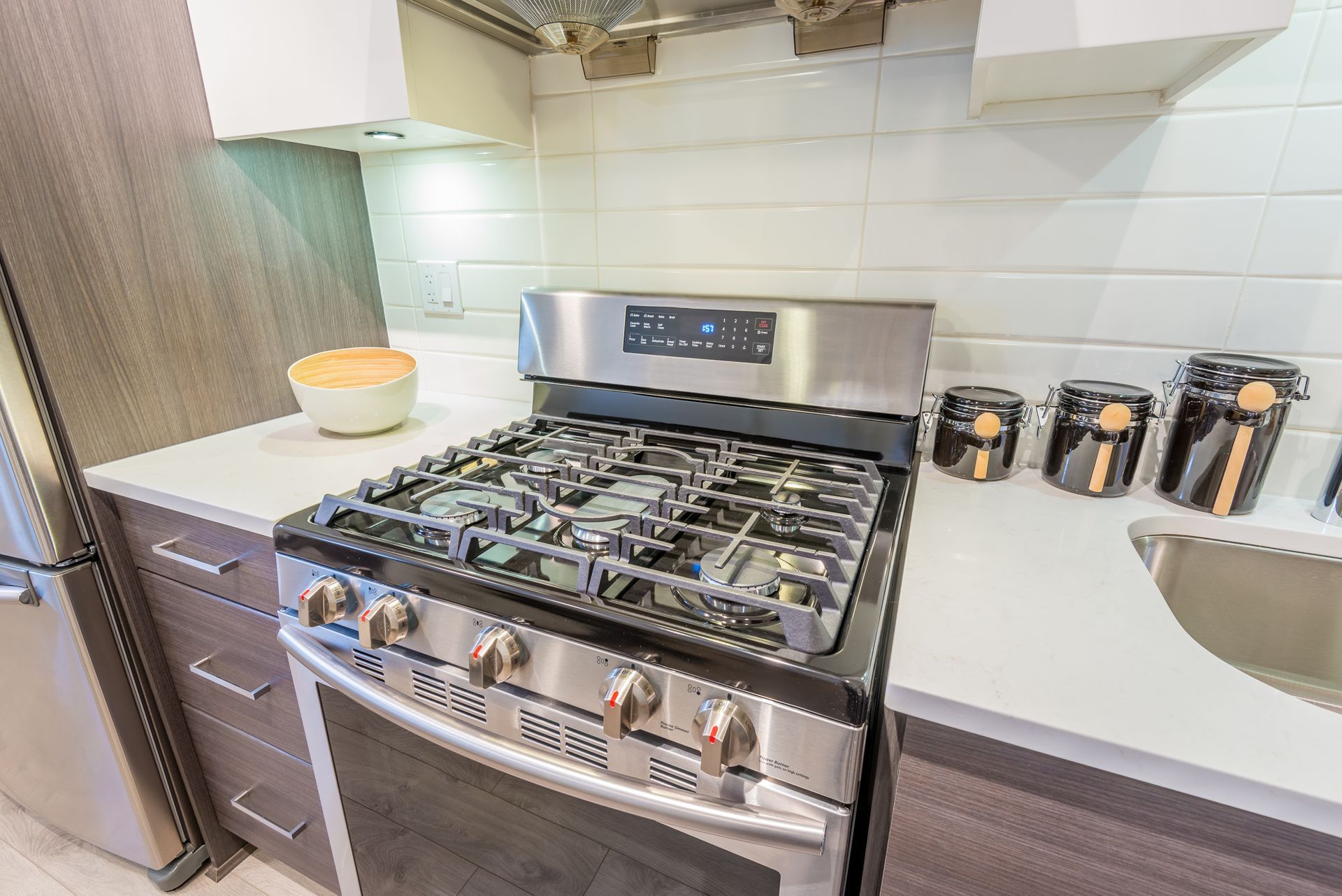 Modern kitchen with stainless steel gas stove, white tile backsplash, and countertop canisters