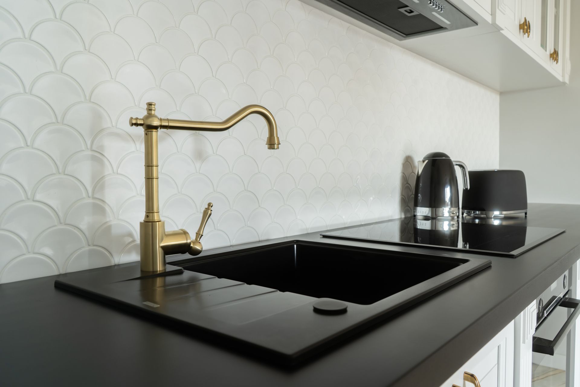 Modern kitchen countertop with matte black sink, gold faucet, and electric kettle and toaster on the right