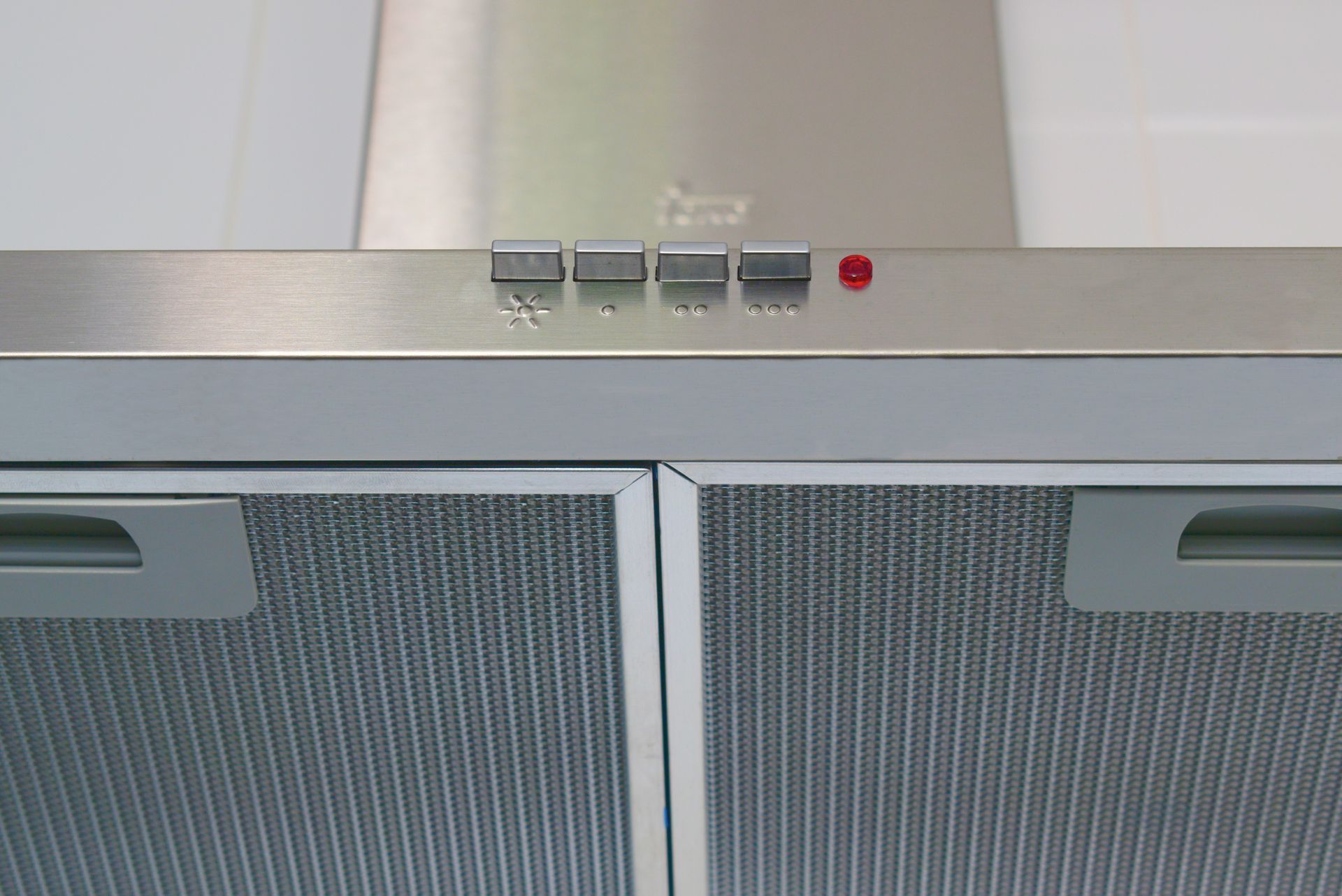 Stainless steel kitchen range hood above two gray mesh cabinet doors